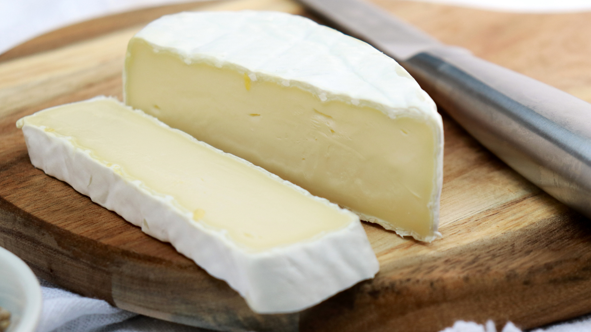 Zwei Stücke Weichkäse auf einem Holzbrett mit Messer.