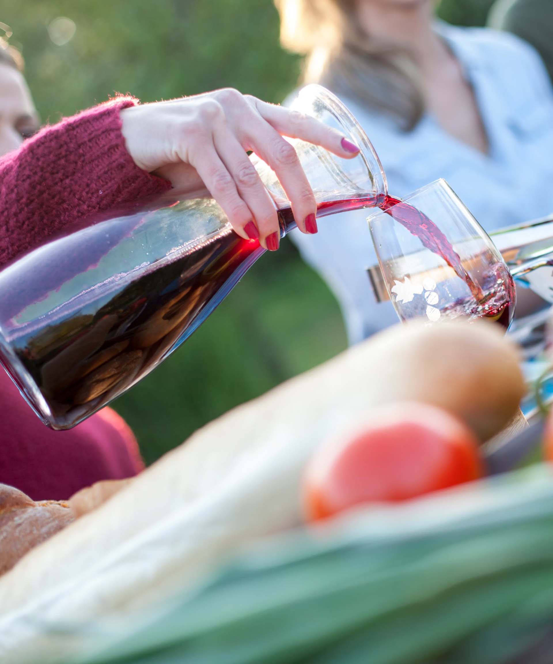 Bei einem geselligen Essen im Freien wird Rotwein aus einer Karaffe in ein Glas gegossen.