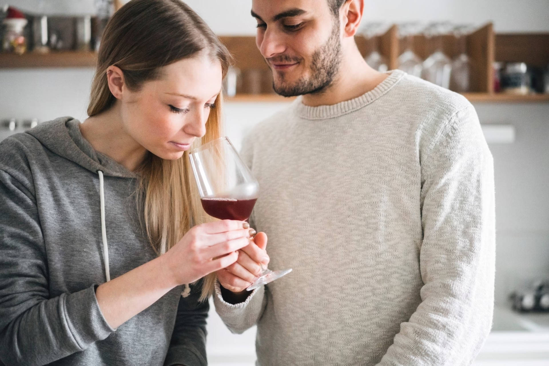 Eine Frau riecht in ein Glas Rotwein. Der Mann daneben schaut ihr dabei zu.