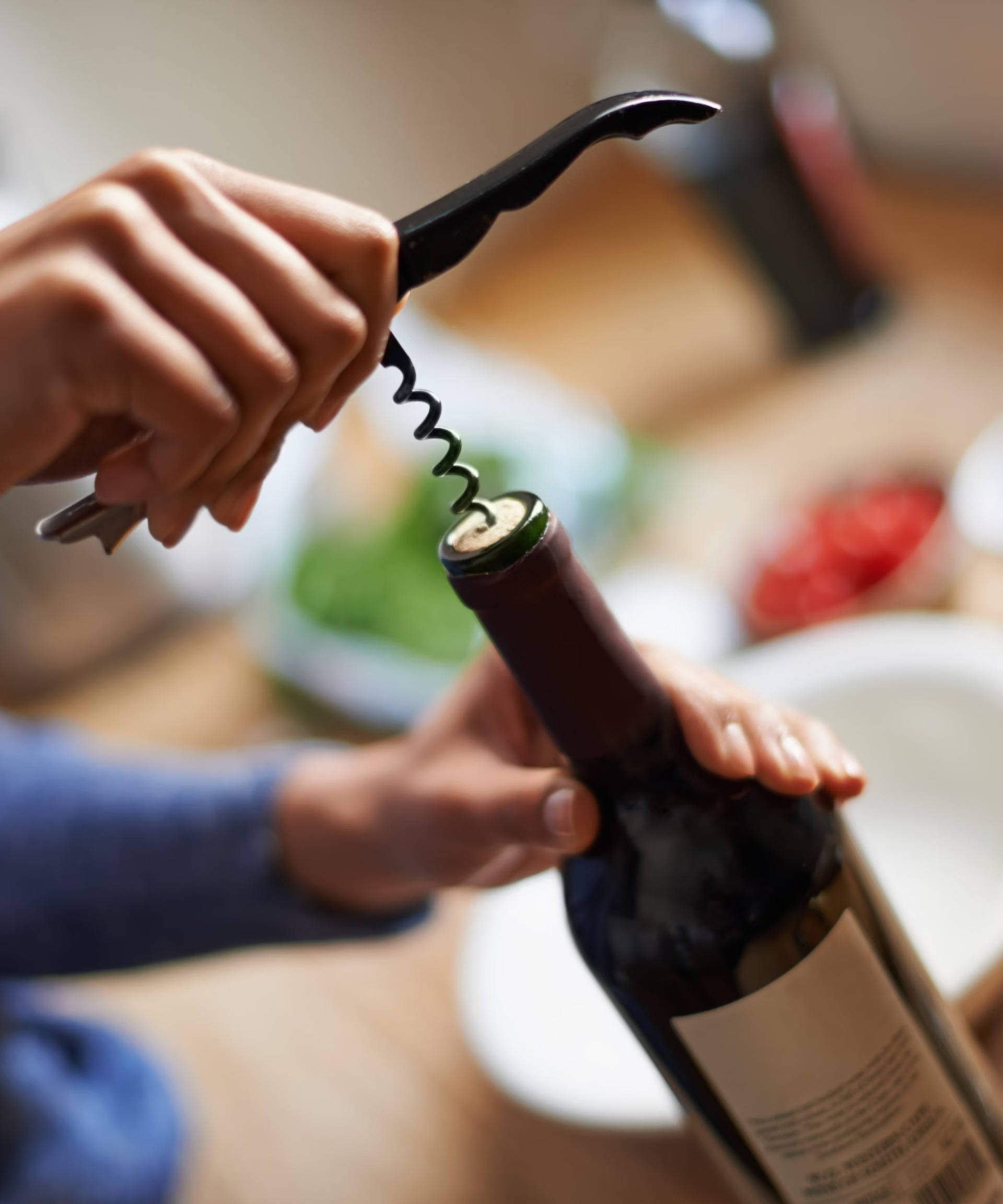 Jemand löst den Korken einer Flasche Rotwein mit einem Korkenzieher. 