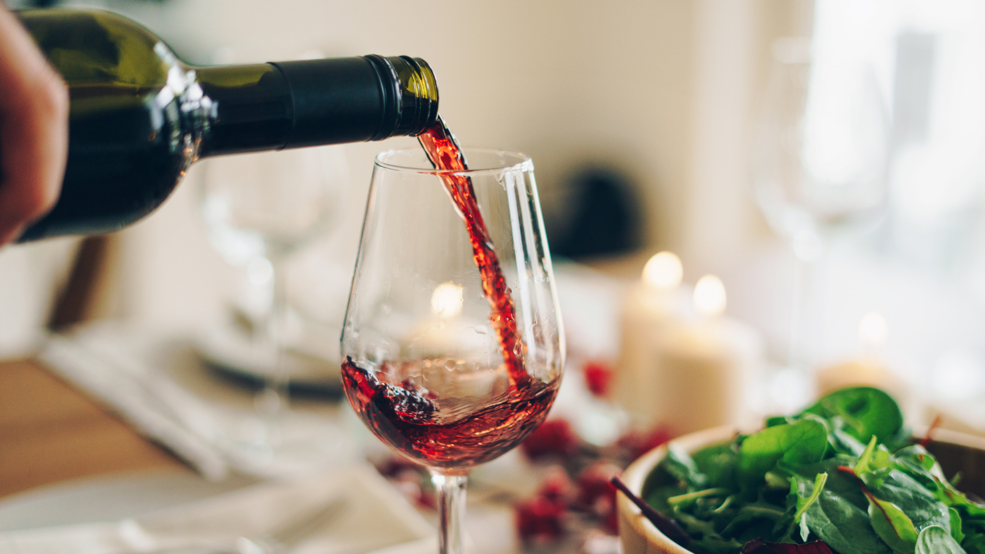 Rotwein wird aus Flasche in Glas geschenkt.