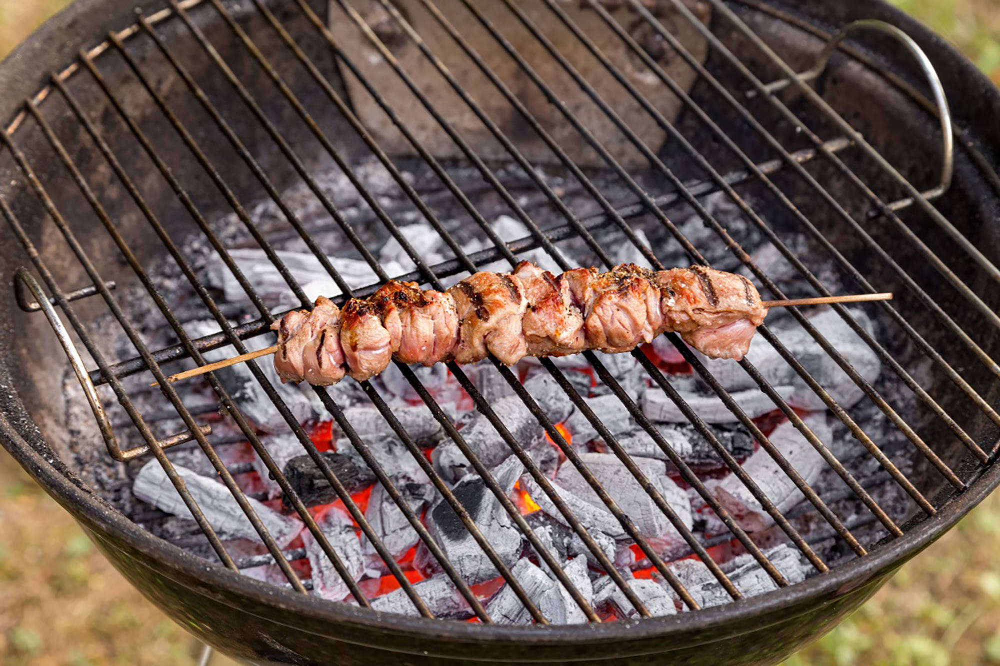 Gegrillter Fleischspieß auf Grillrost mit glühender Kohle im Freien.
