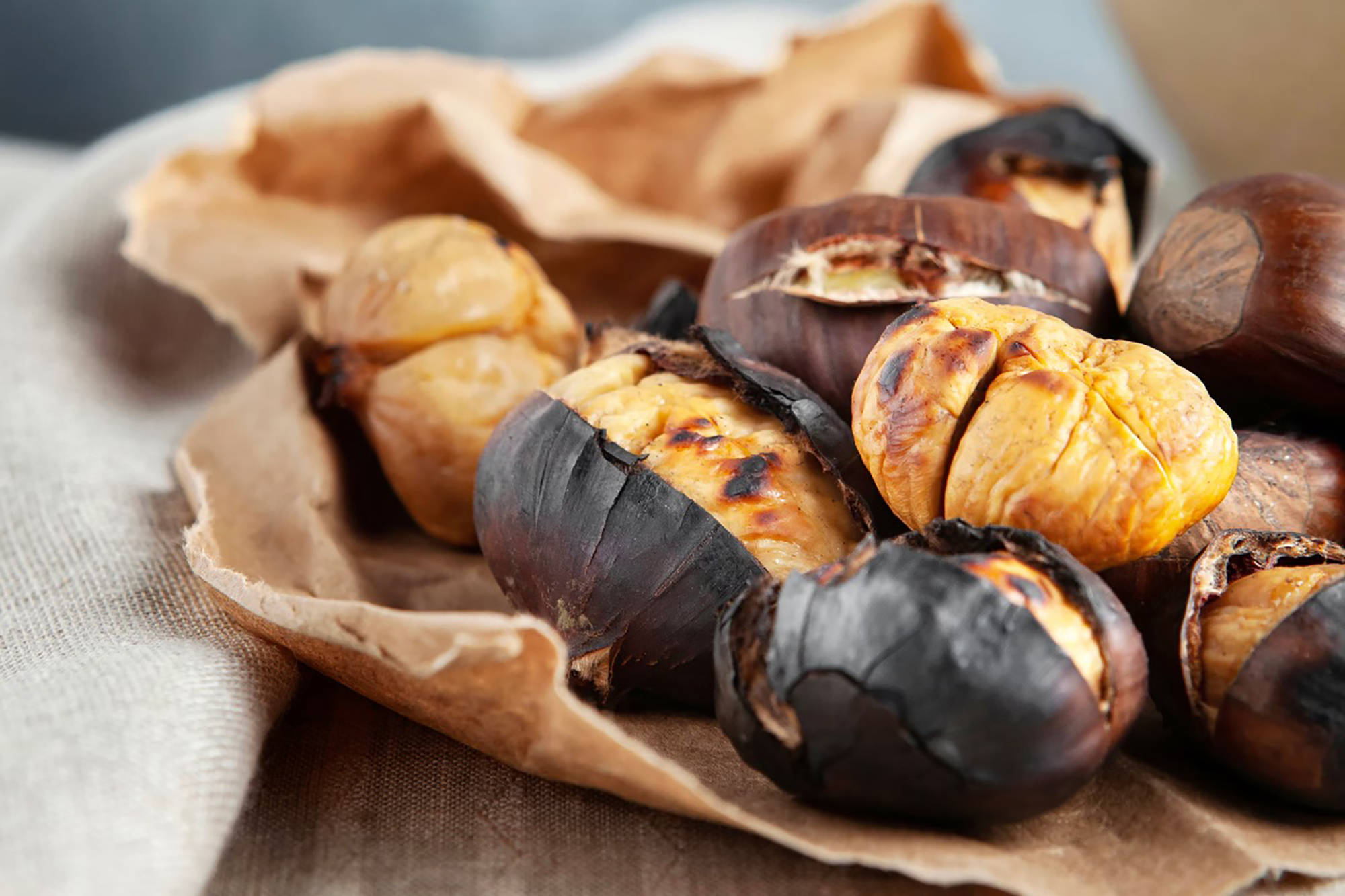 Knusprig geröstete Maronen mit aufgesprungener Schale, serviert auf braunem Papier.