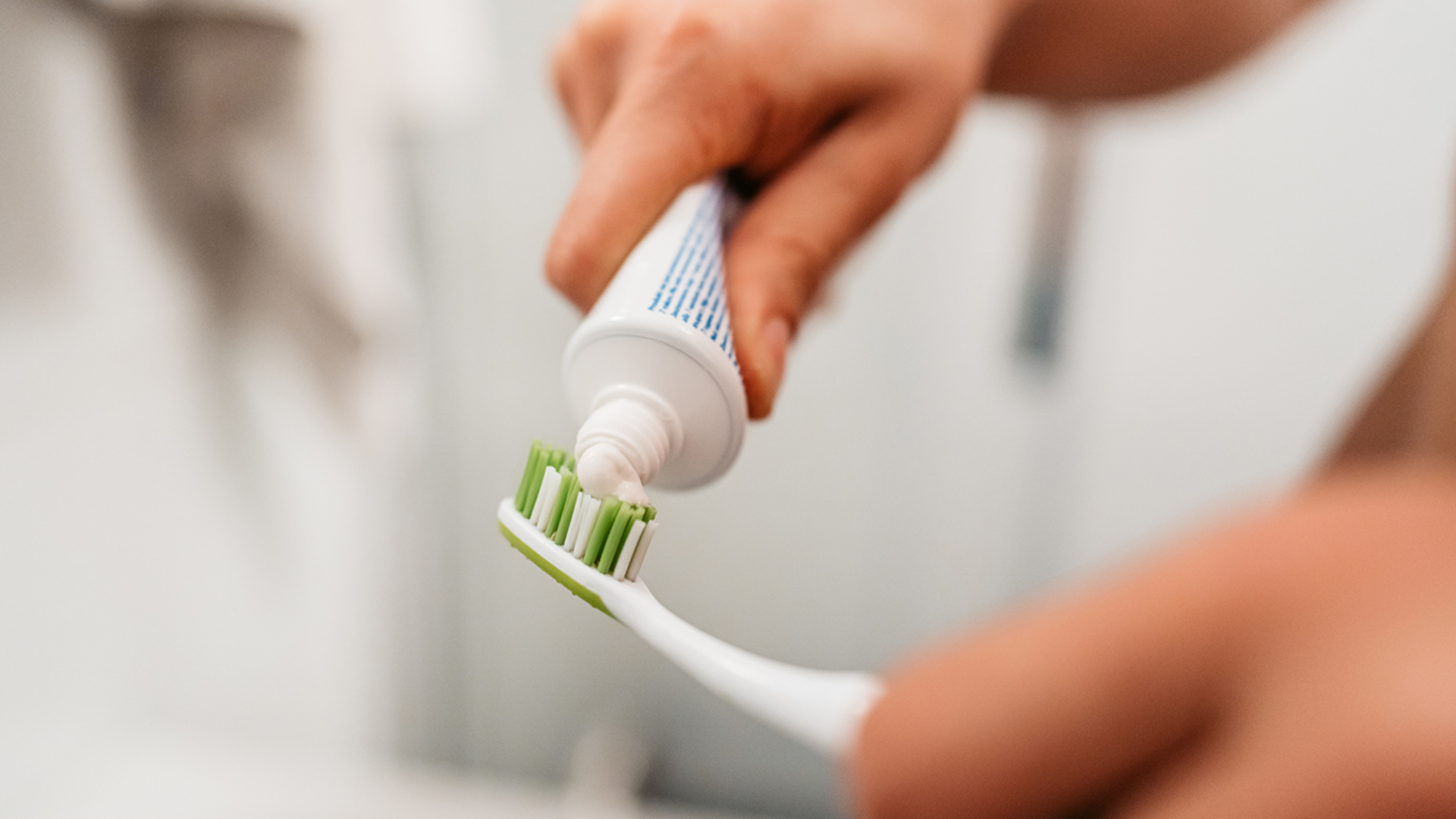 Hand drückt Zahnpasta auf grüne Zahnbürste.