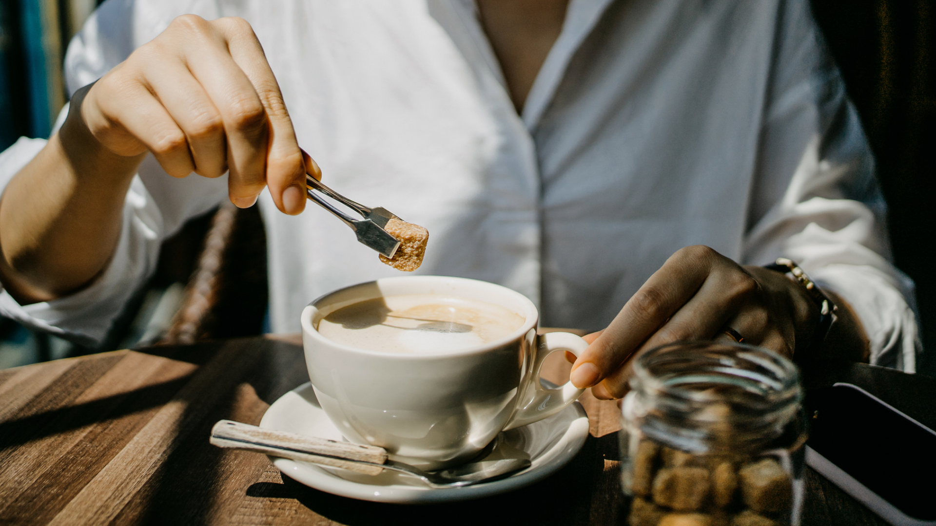 Zuckerwürfel mit Zange wird in eine Tasse Kaffee gegeben.