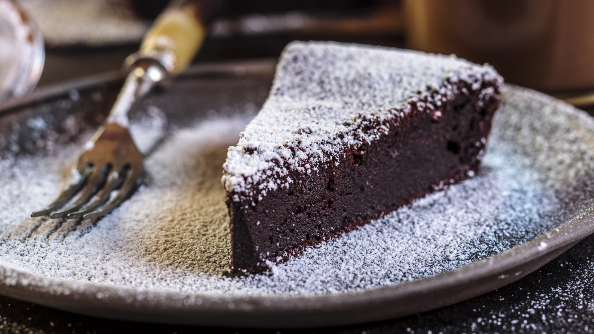 Schokoladenkuchenstück mit Puderzucker auf einem Teller mit Gabel.