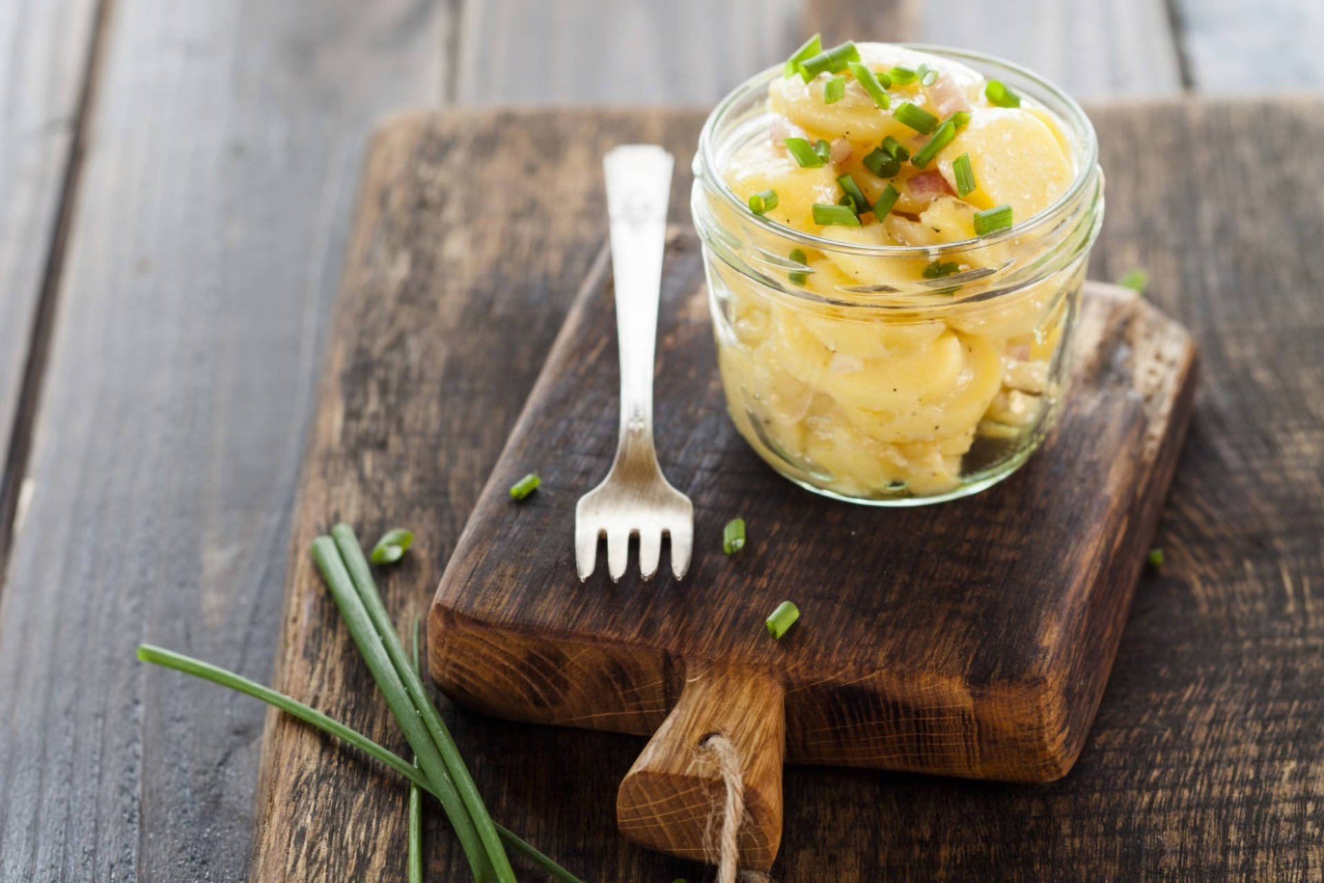 Kartoffelsalat im Glas mit Schnittlauch auf Holzbrett.
