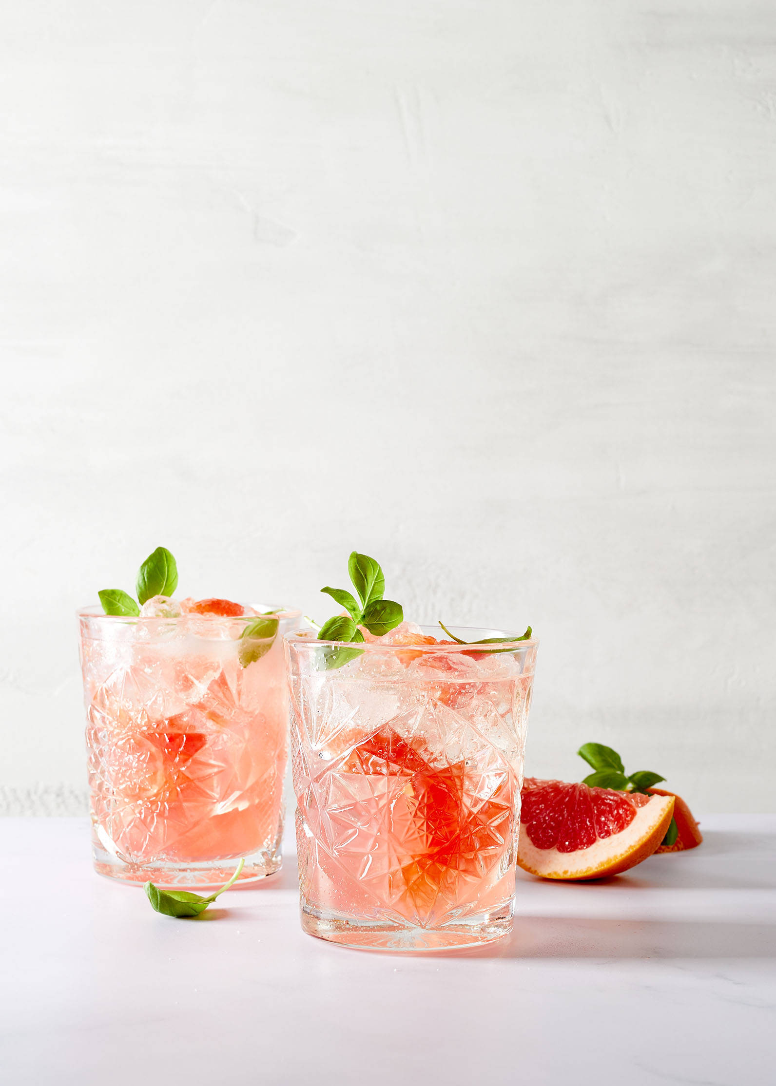 Zwei Gläser Cocktail mit Grapefruit und Basilikum.
