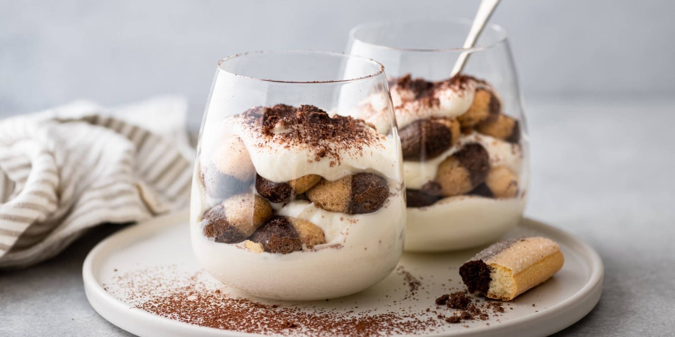 Zwei Schichtdesserts mit Löffelbiskuits, Creme und Kakao.