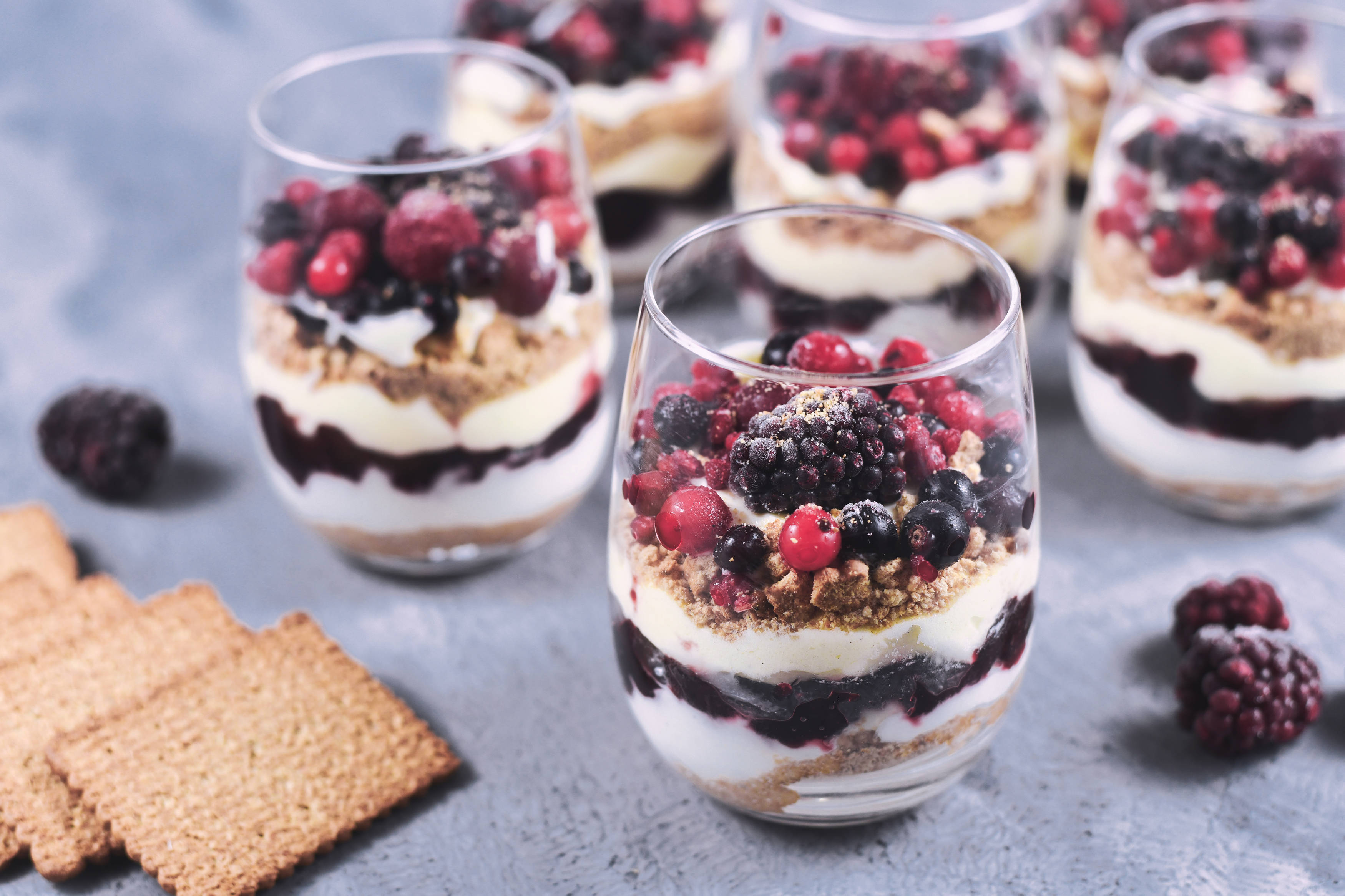 Geschichtete Desserts im Glas mit Beeren und Keksen.