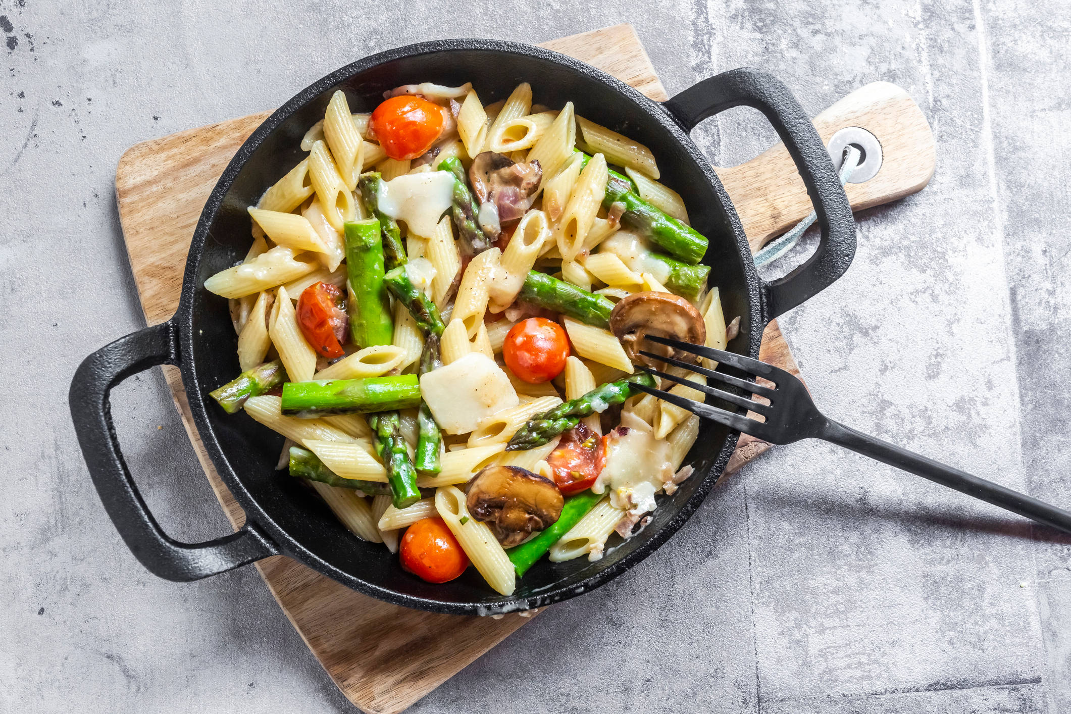 Pasta mit Spargel, Tomaten und Pilzen in Pfanne.