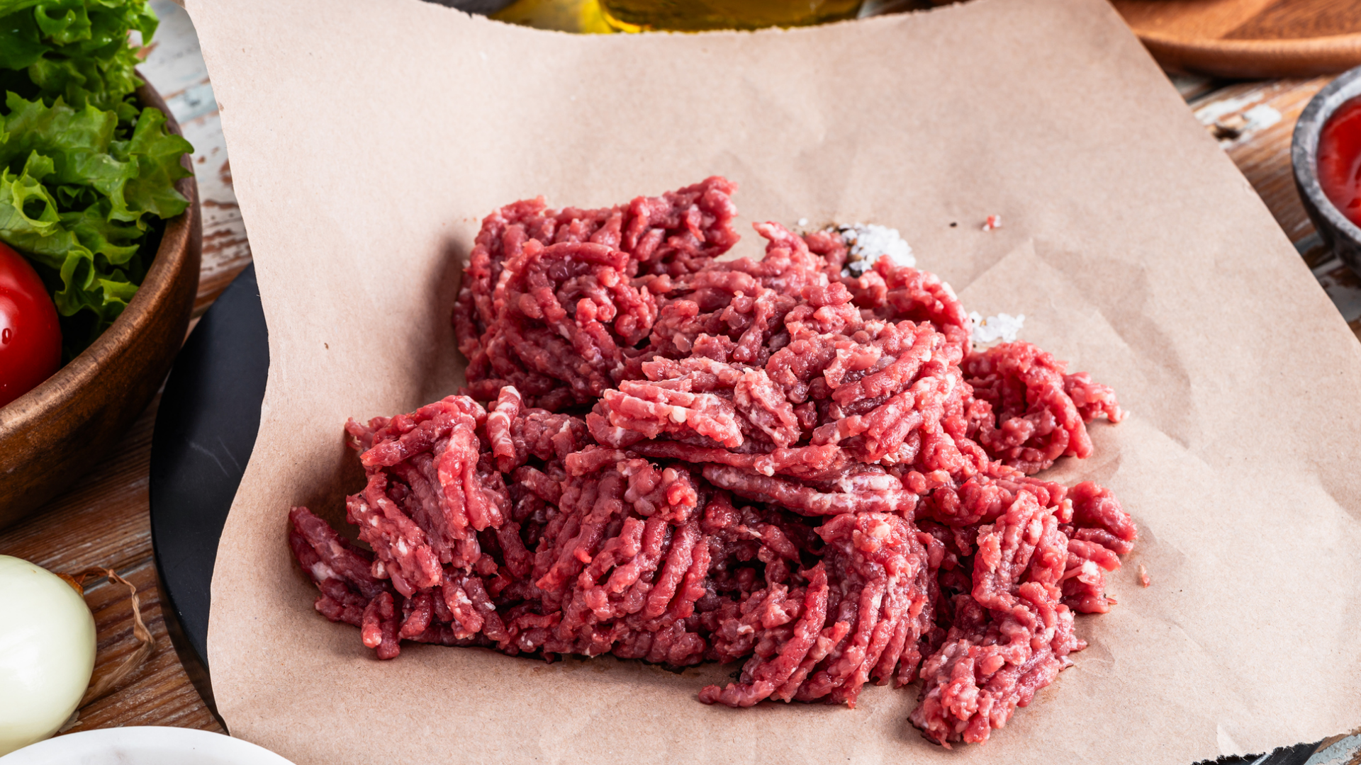 Rohes Rinderhackfleisch auf Backpapier mit Gewürzen und Gemüse.