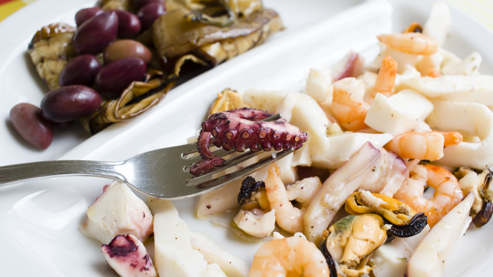 Teller mit Meeresfrüchtesalat, Oliven und gegrillter Aubergine.