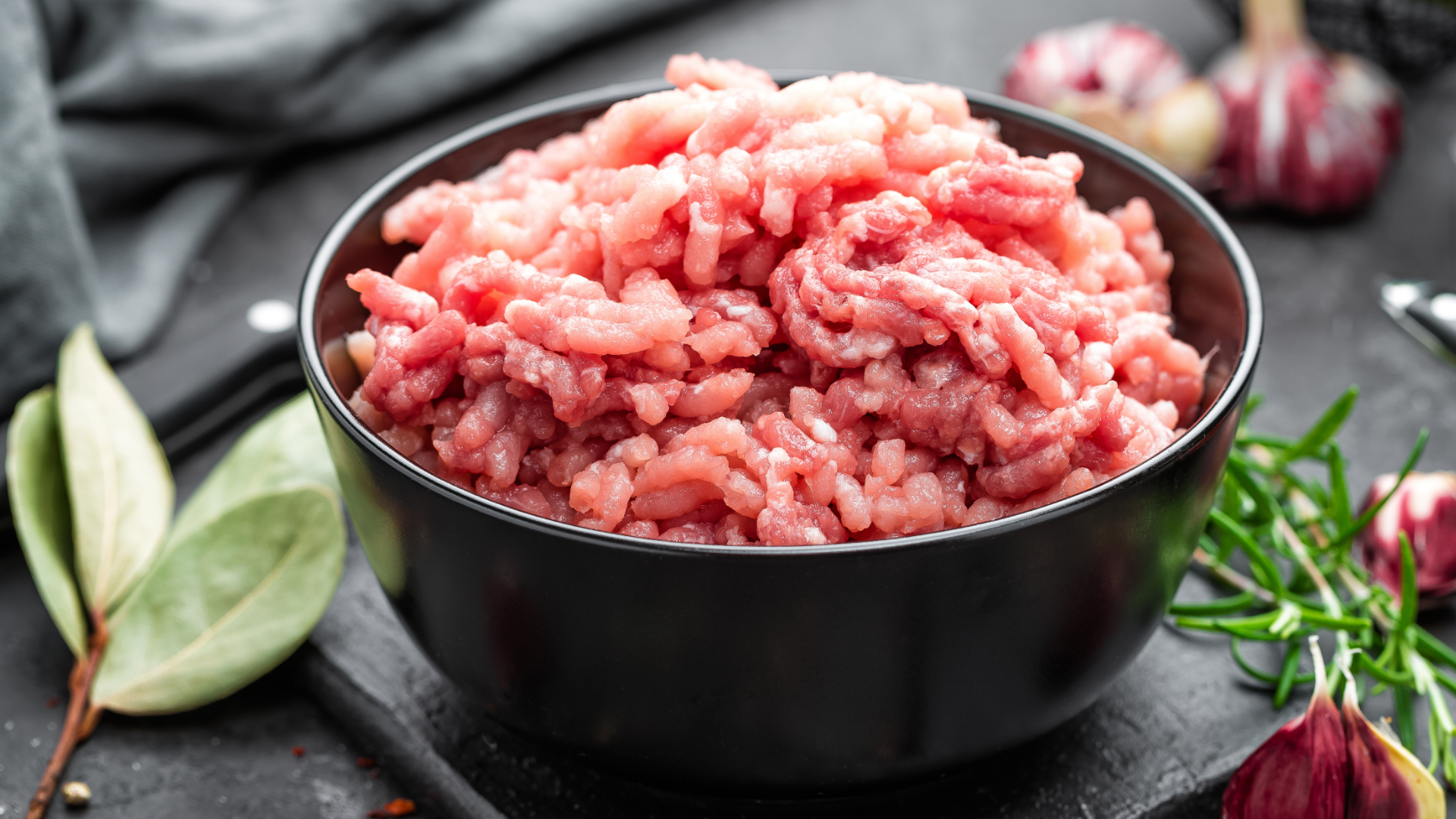 Schale mit rohem Hackfleisch, daneben Kräuter und Knoblauch.