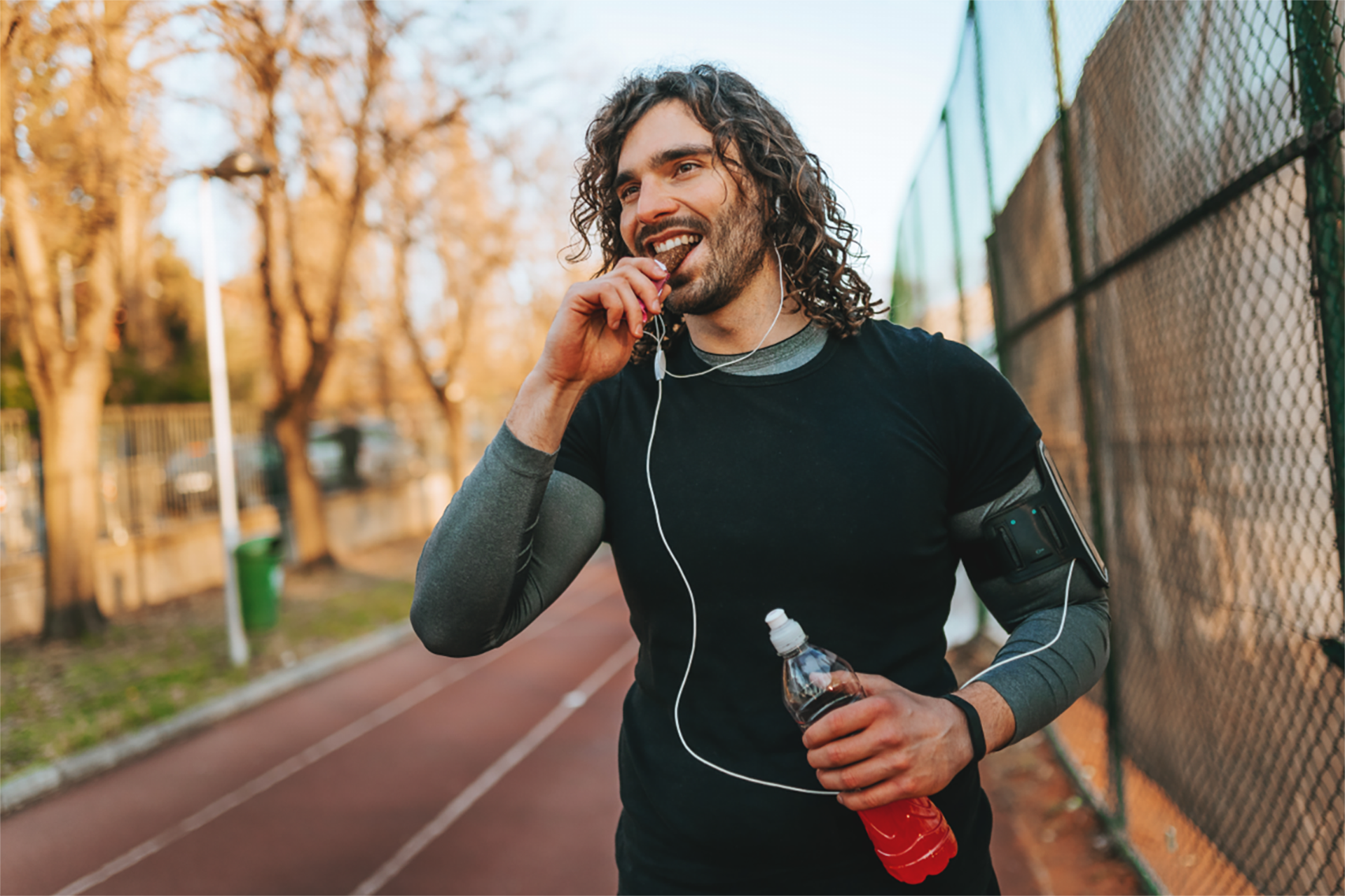 Jogger beißt in einen Energieriegel und hält eine Getränkeflasche, während er auf einer Laufbahn trainiert.