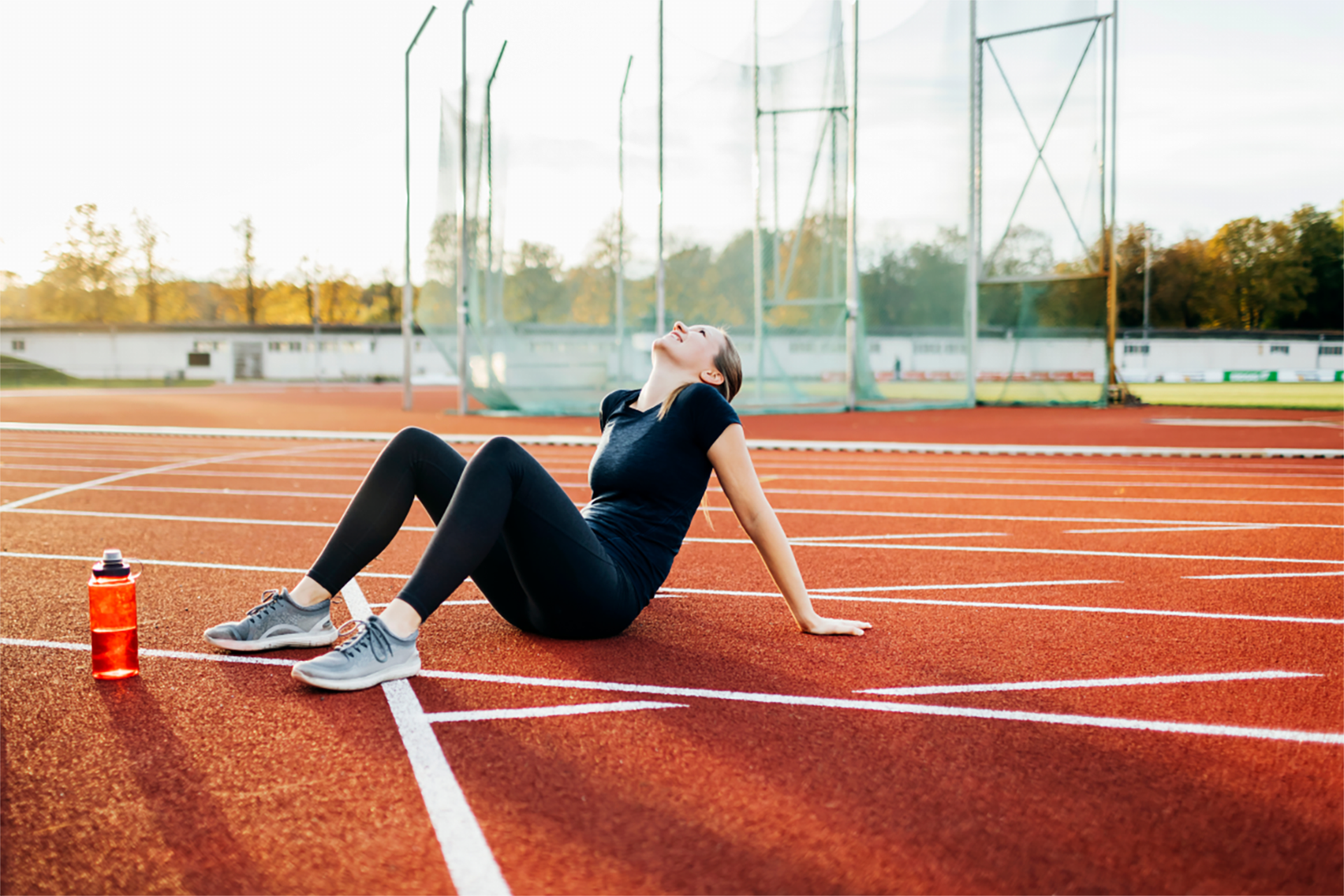Frau in Sportkleidung sitzt auf einer Laufbahn und erholt sich nach einem intensiven Training, neben ihr eine Wasserflas