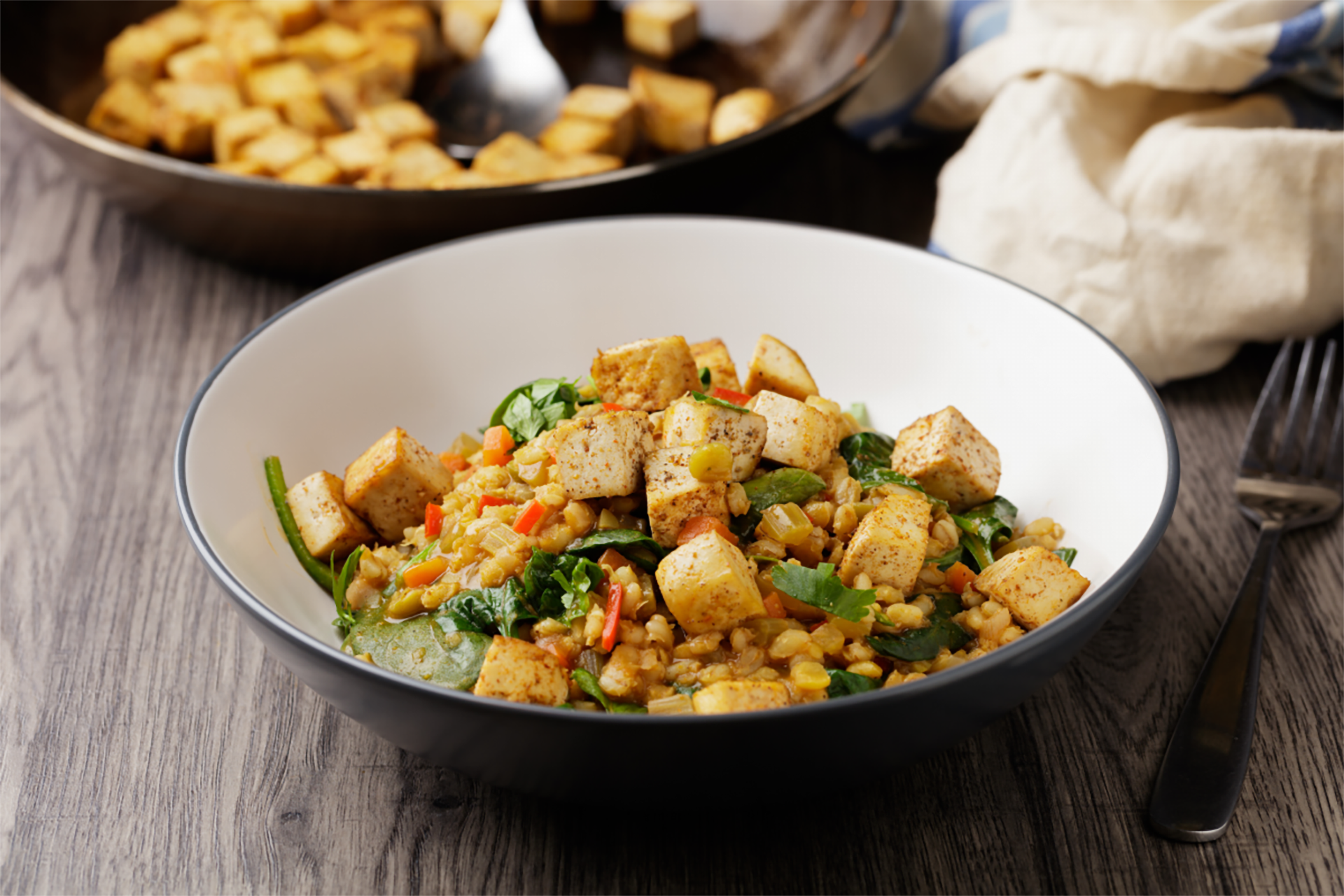 Schüssel mit gebratenem Tofu, Gemüse und Linsen, serviert auf einem Holztisch.