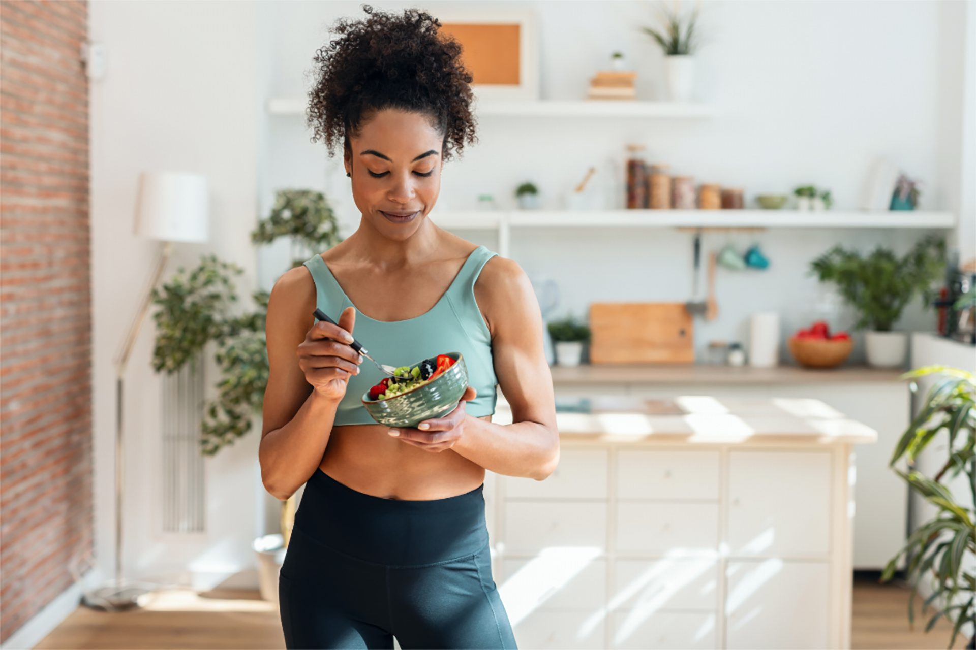 Frau in Sportkleidung isst eine selbstgemachte Bowl in einer modernen Küche nach dem Training.