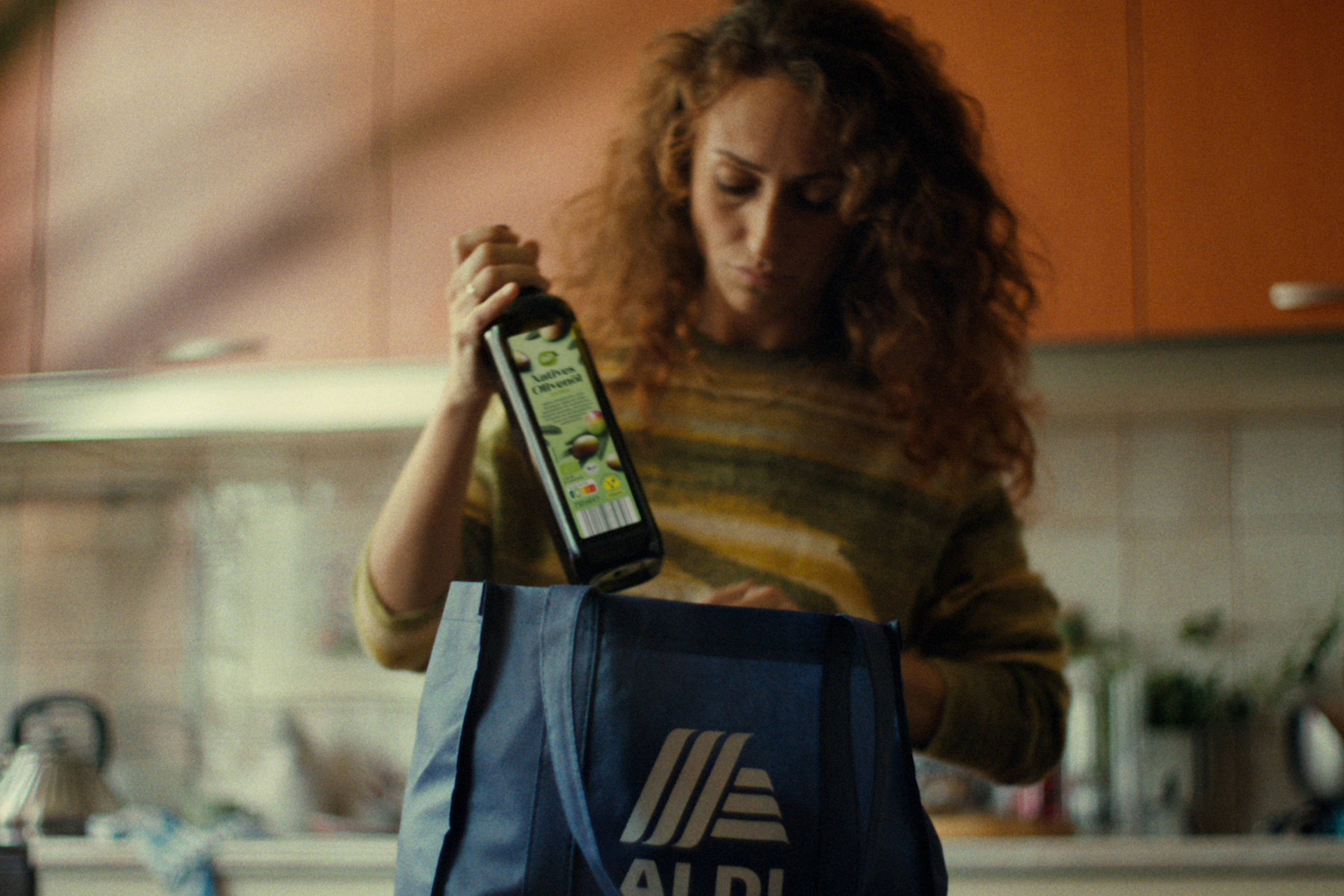 Eine Frau füllt eine ALDI SÜD Einkaufstasche mit Lebensmitteln, darunter eine Flasche Olivenöl.