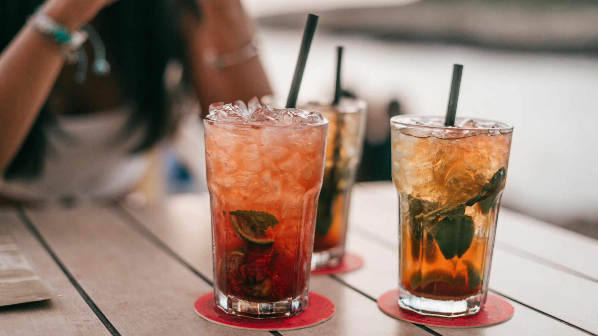 Drei Eistees mit Strohhalm auf Tisch, Person im Hintergrund.
