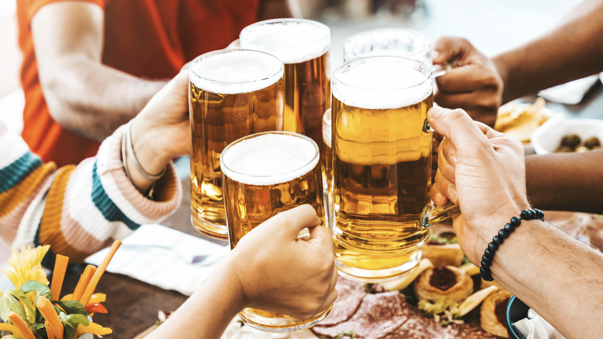 Anstossen mit Bierkrügen über einem Tisch mit Speisen.