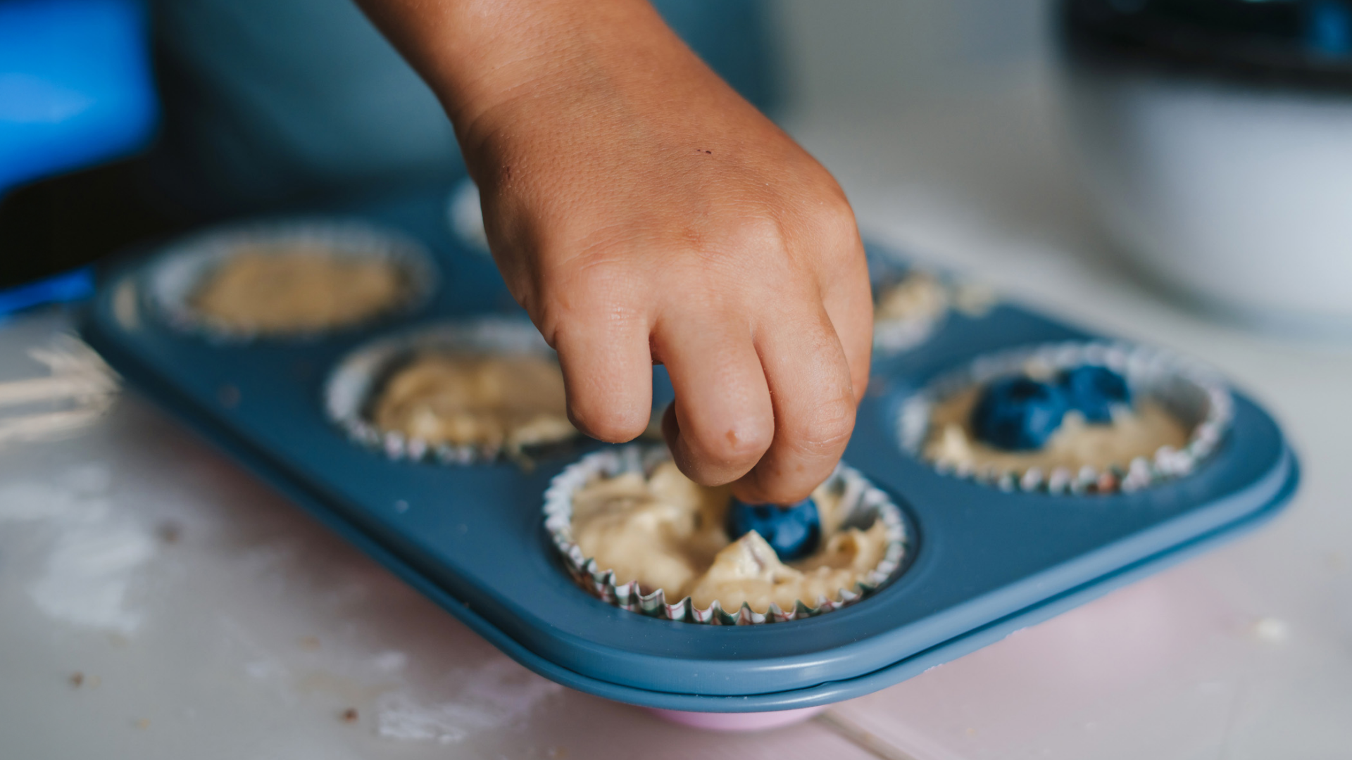 Kind legt Blaubeeren in Muffinteig.