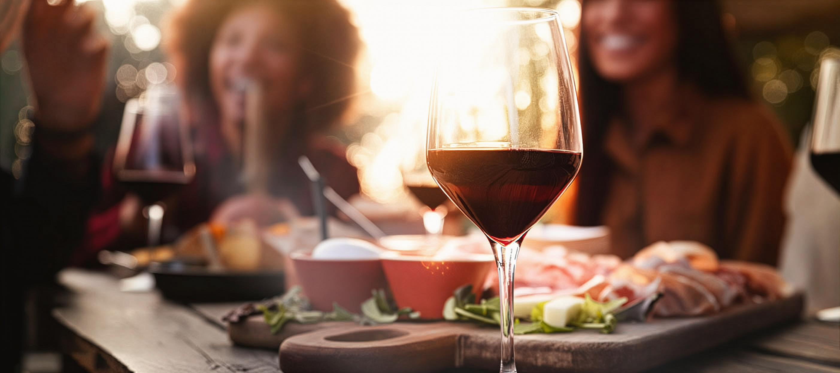 Eine Gruppe Menschen sitzt an einem Tisch, auf dem Tisch stehen einige Gläser Rotwein und Essen.