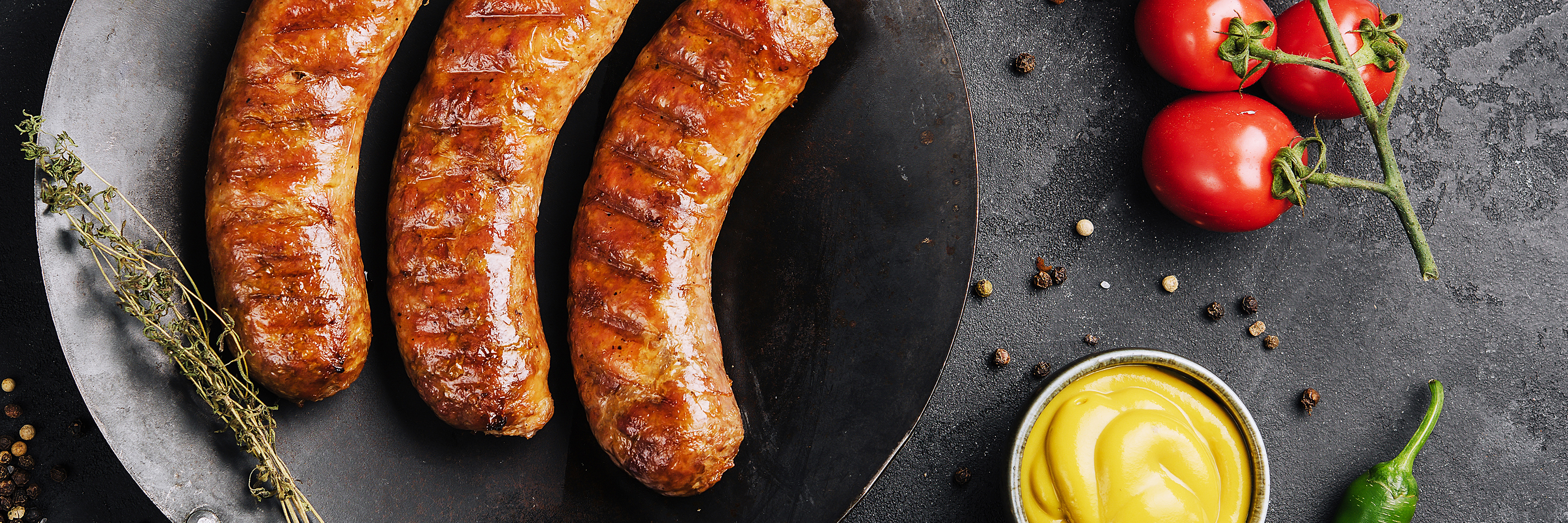 Rohe Bratwürste mit Rosmarin auf Packpapier.