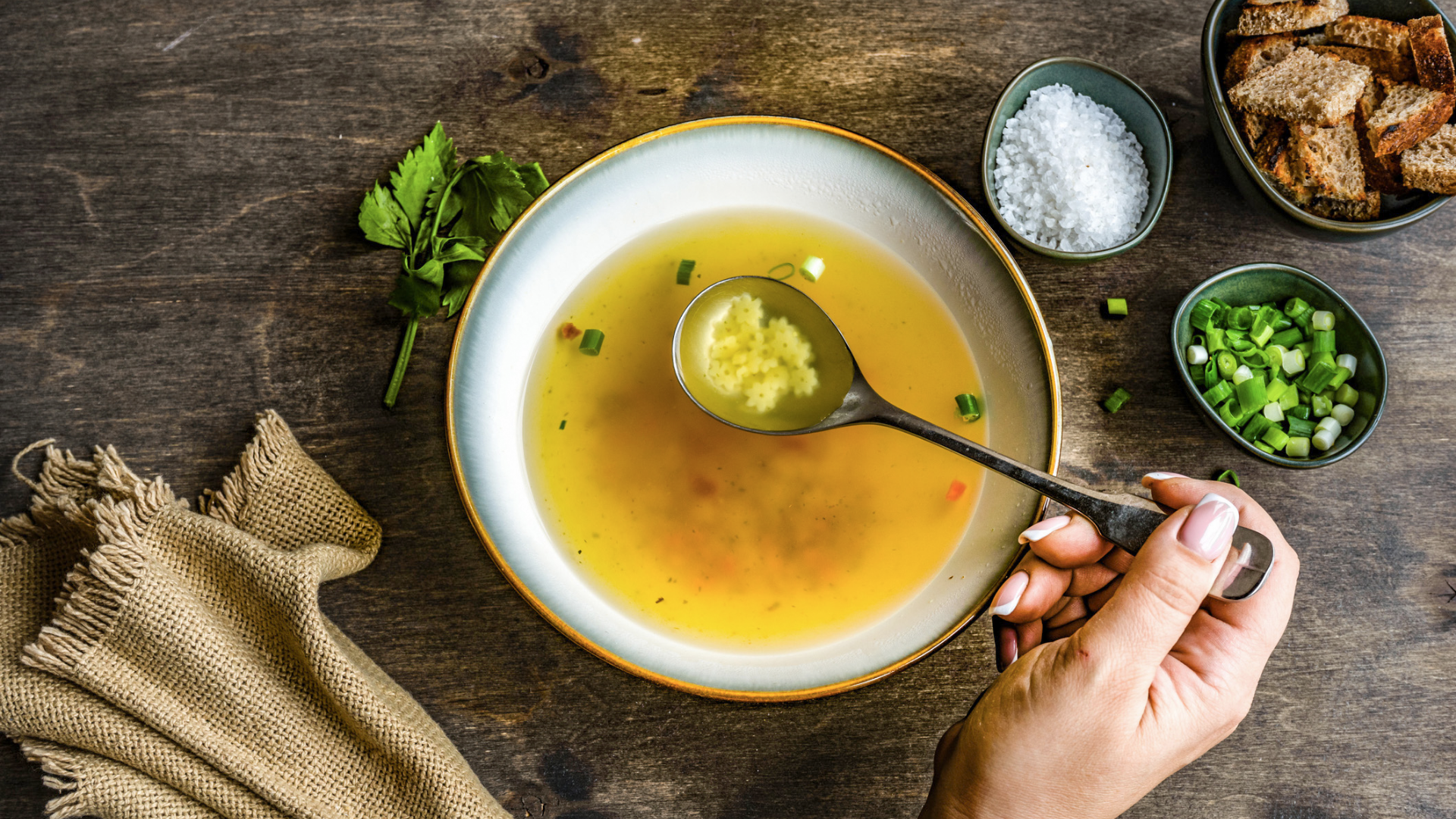 Schale mit Brühe, Sternchennudeln und Beilagen auf Holztisch.