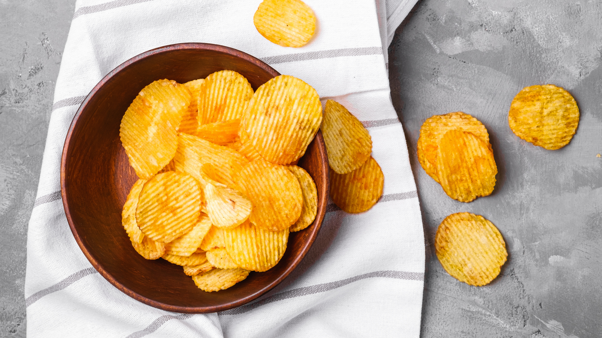 Geriffelte Kartoffelchips in Holzschale auf Küchentuch.