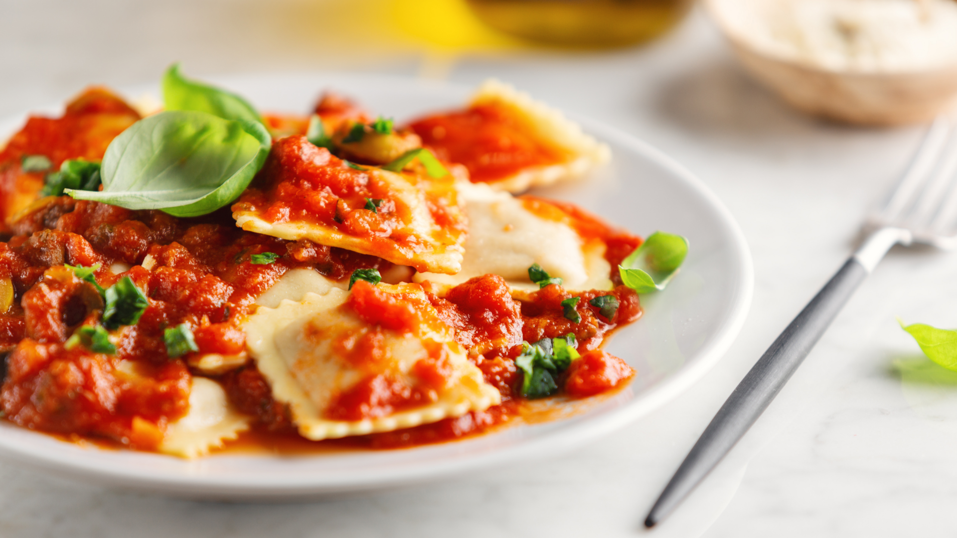 Teller mit Ravioli und Tomatensoße, Basilikum.