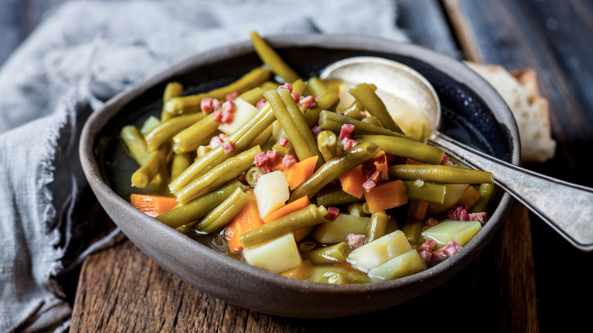 Bohneneintopf mit Speck, Karotten und Kartoffeln in Schüssel.