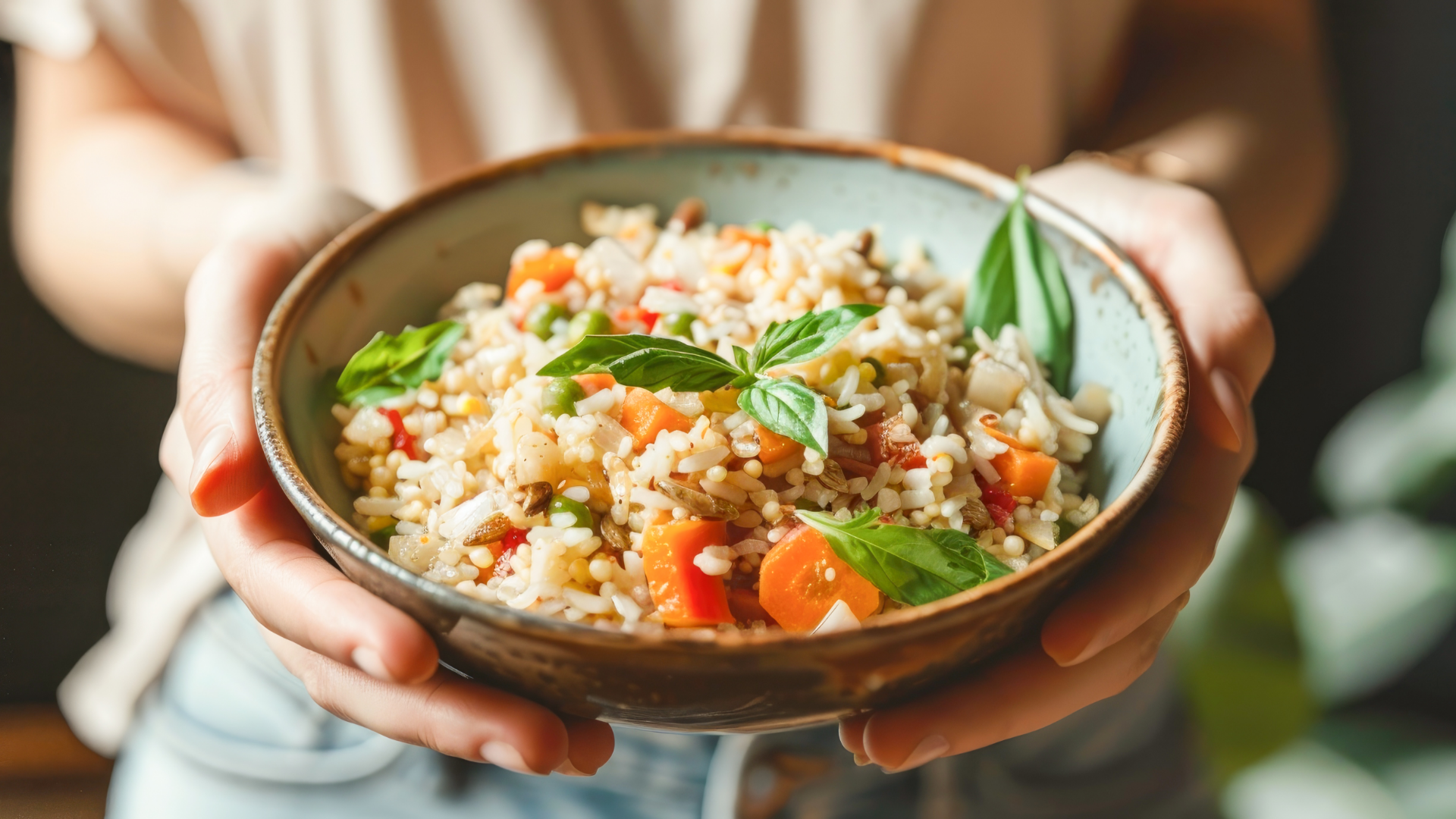 Hände halten Schale mit Reis, Gemüse und Basilikum.