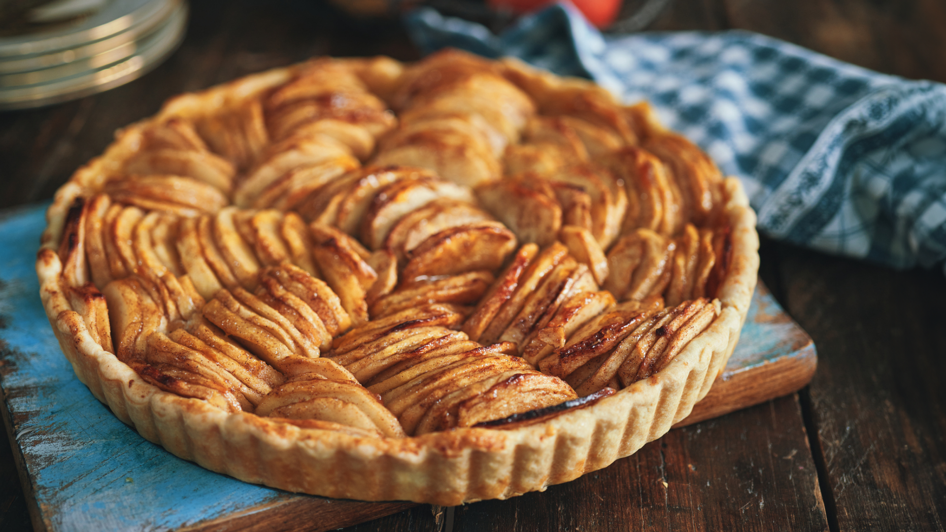 Apfeltarte mit goldenen Apfelscheiben auf Holzbrett.