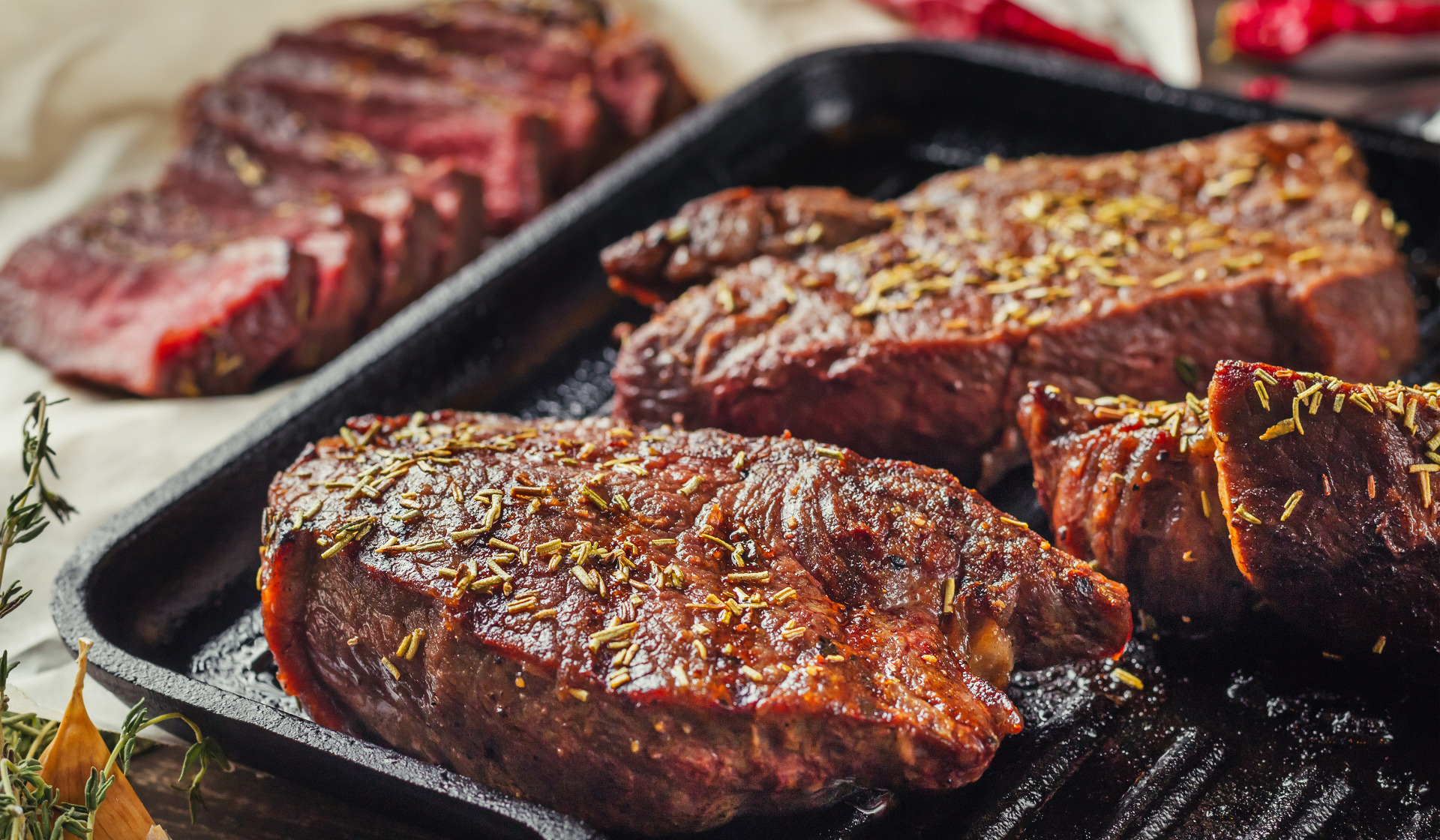 Drei gebratene und mit Kräutern marinierte Rindfleischstücke in einer Bratpfanne.