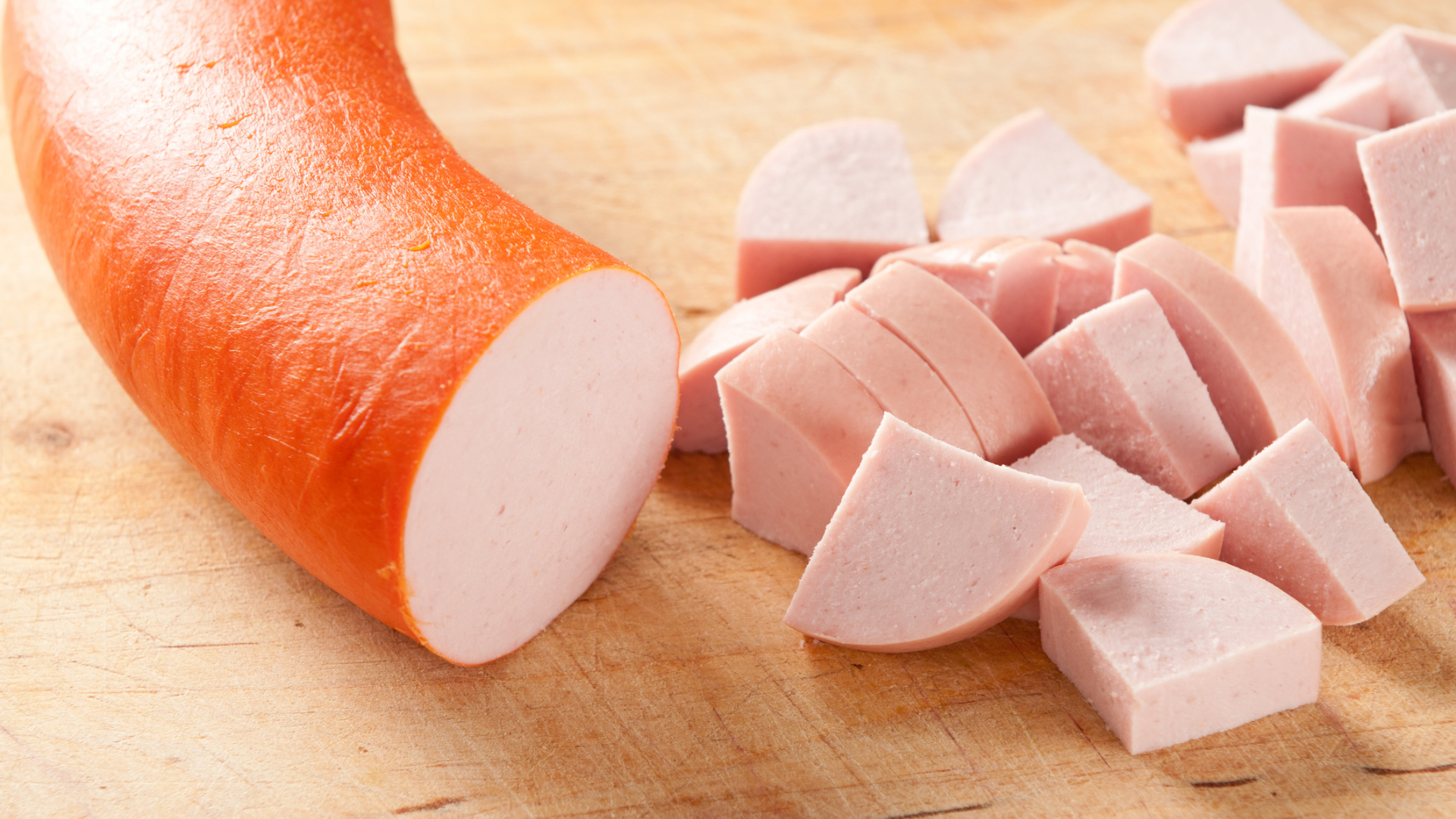 Ganze und geschnittene Fleischwurst auf einem Holzbrett.