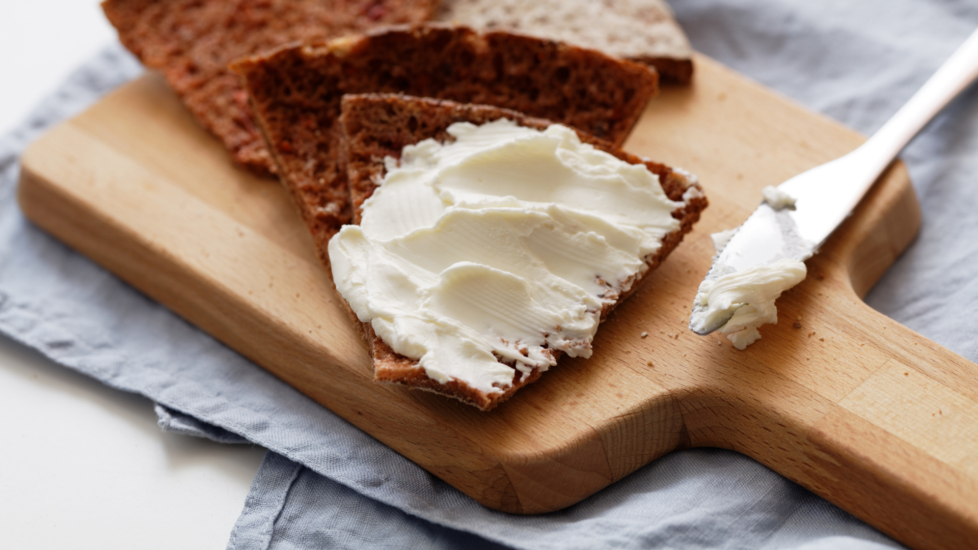 Brot mit Frischkäse auf Holzbrett und Messer.