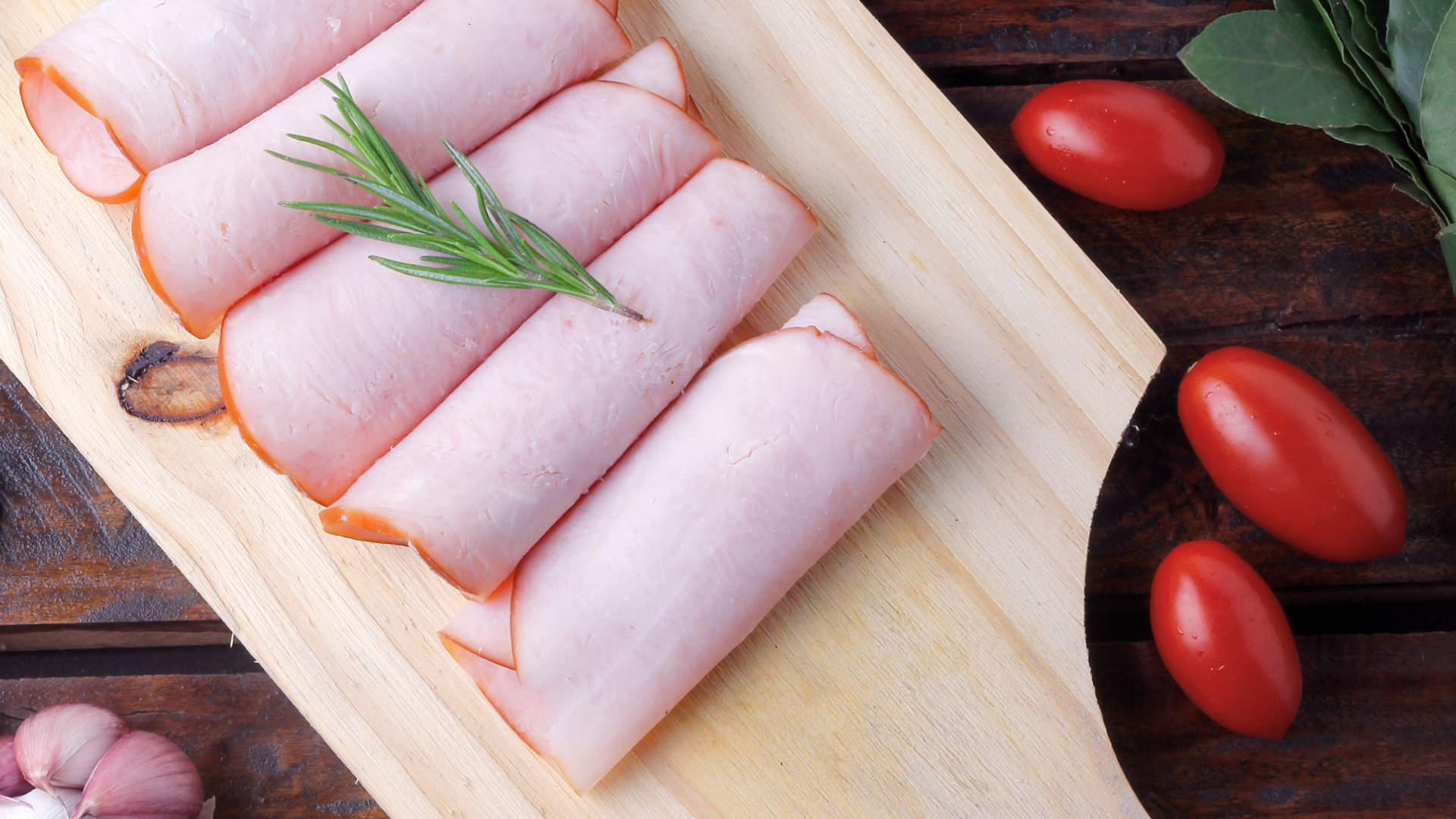 Aufgerollte Geflügelwurstscheiben mit Rosmarin, Tomaten und Knoblauch.