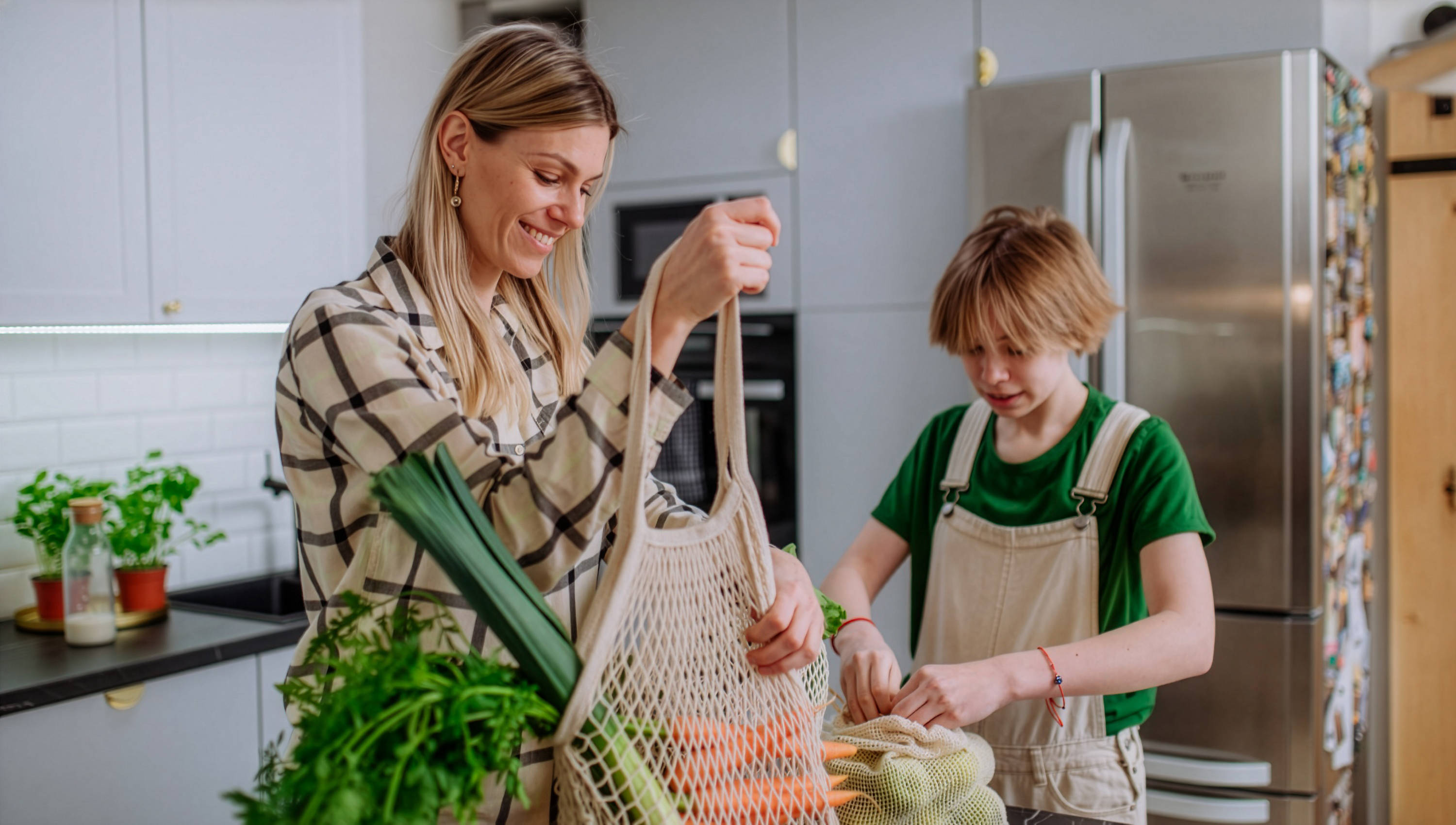  Mutter und Sohn packen Obst und Gemüse das sie eingekauft haben in der Küche aus.