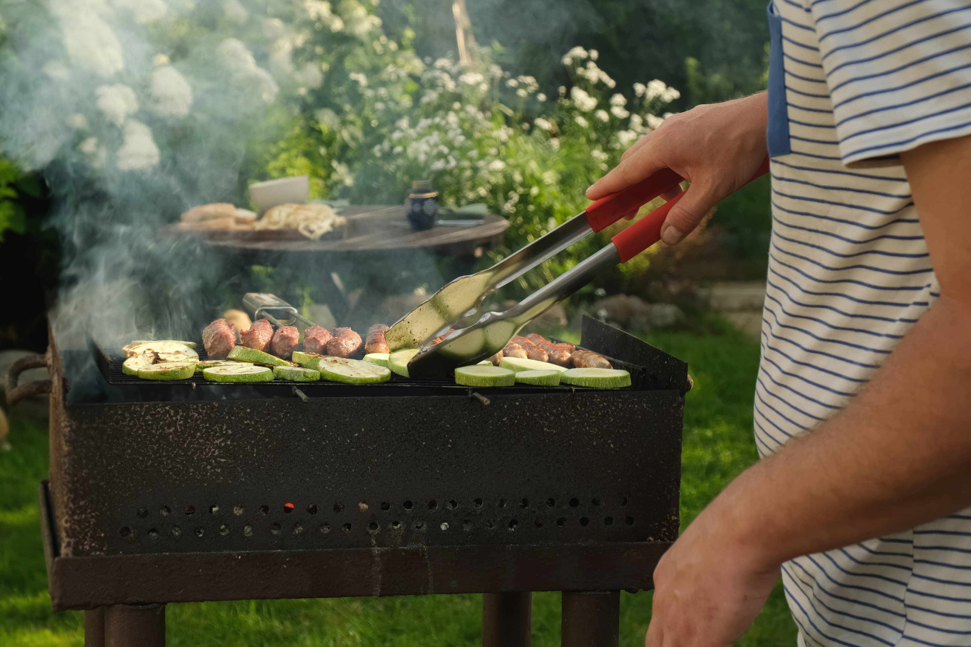 Ein Mann bereitet im Sommer im Garten Essen auf einem Grill zu.