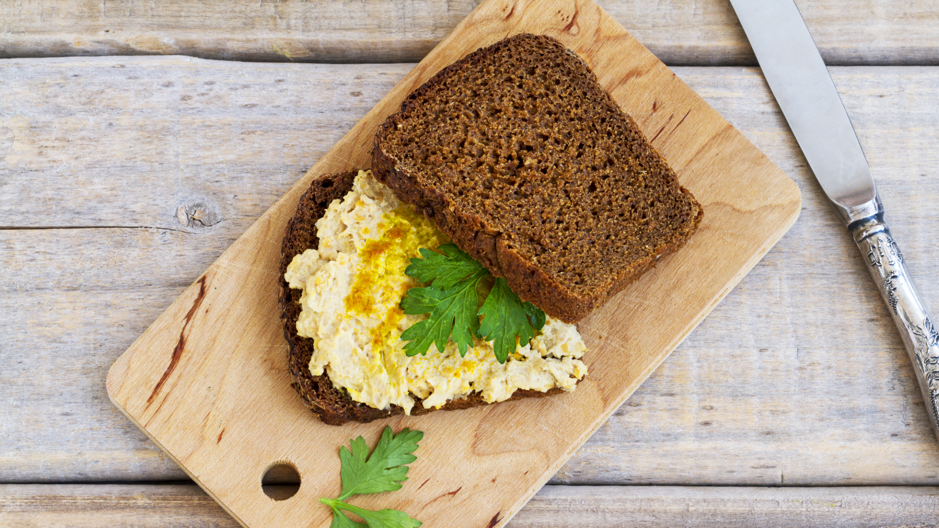 Schwarzbrot mit Brotaufstrich und Petersilie auf Holzbrett.