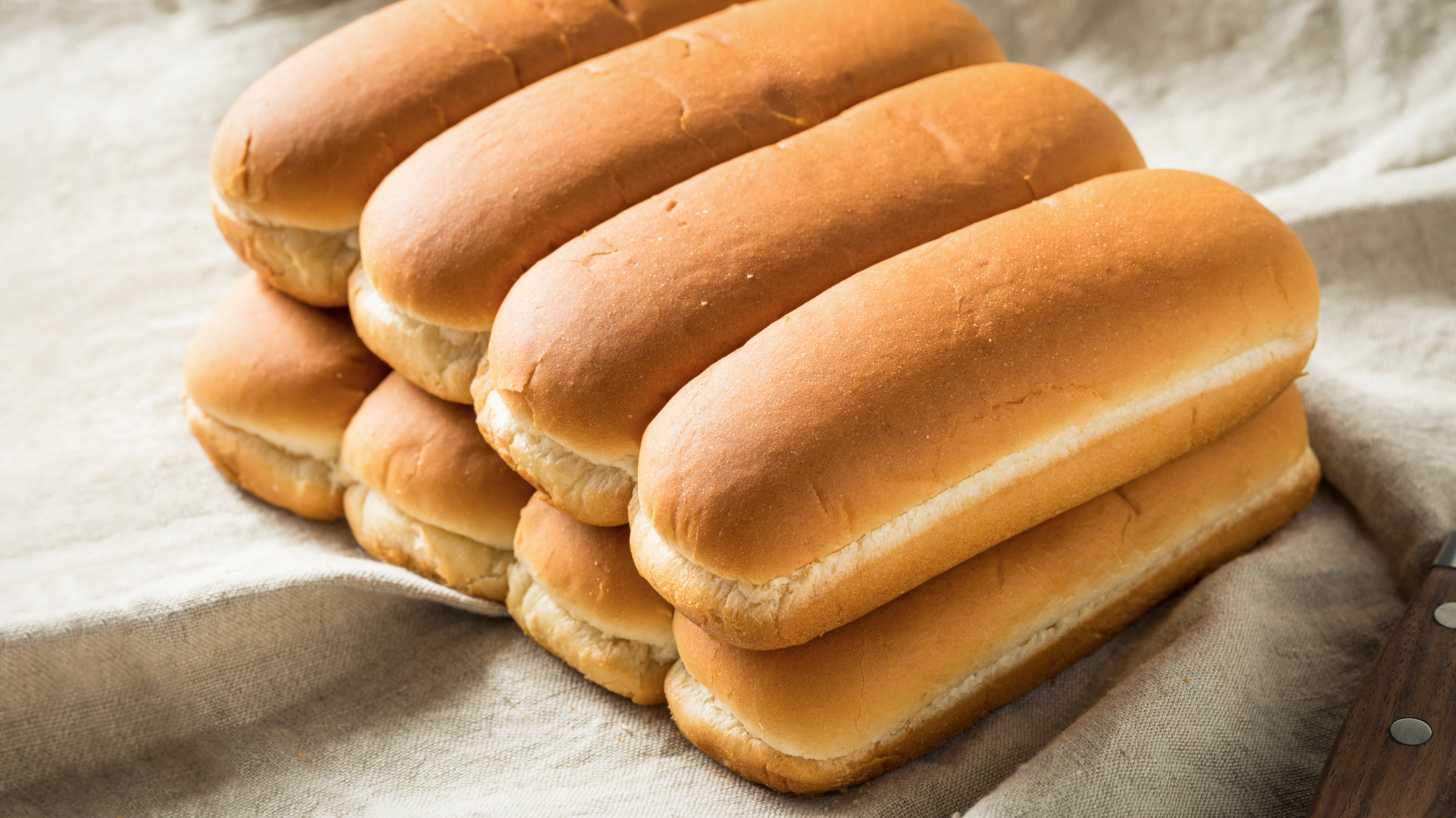 Stapel goldbrauner Hotdog-Brötchen auf hellem Leinentuch.