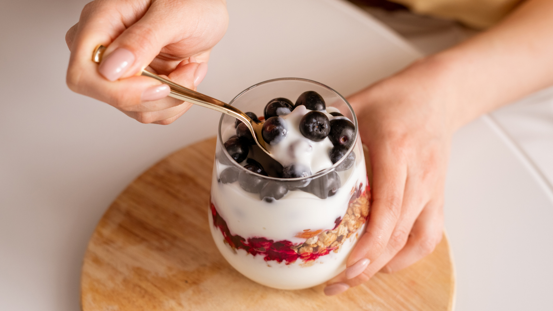 Hände löffeln Joghurt-Parfait mit Heidelbeeren und Müsli.