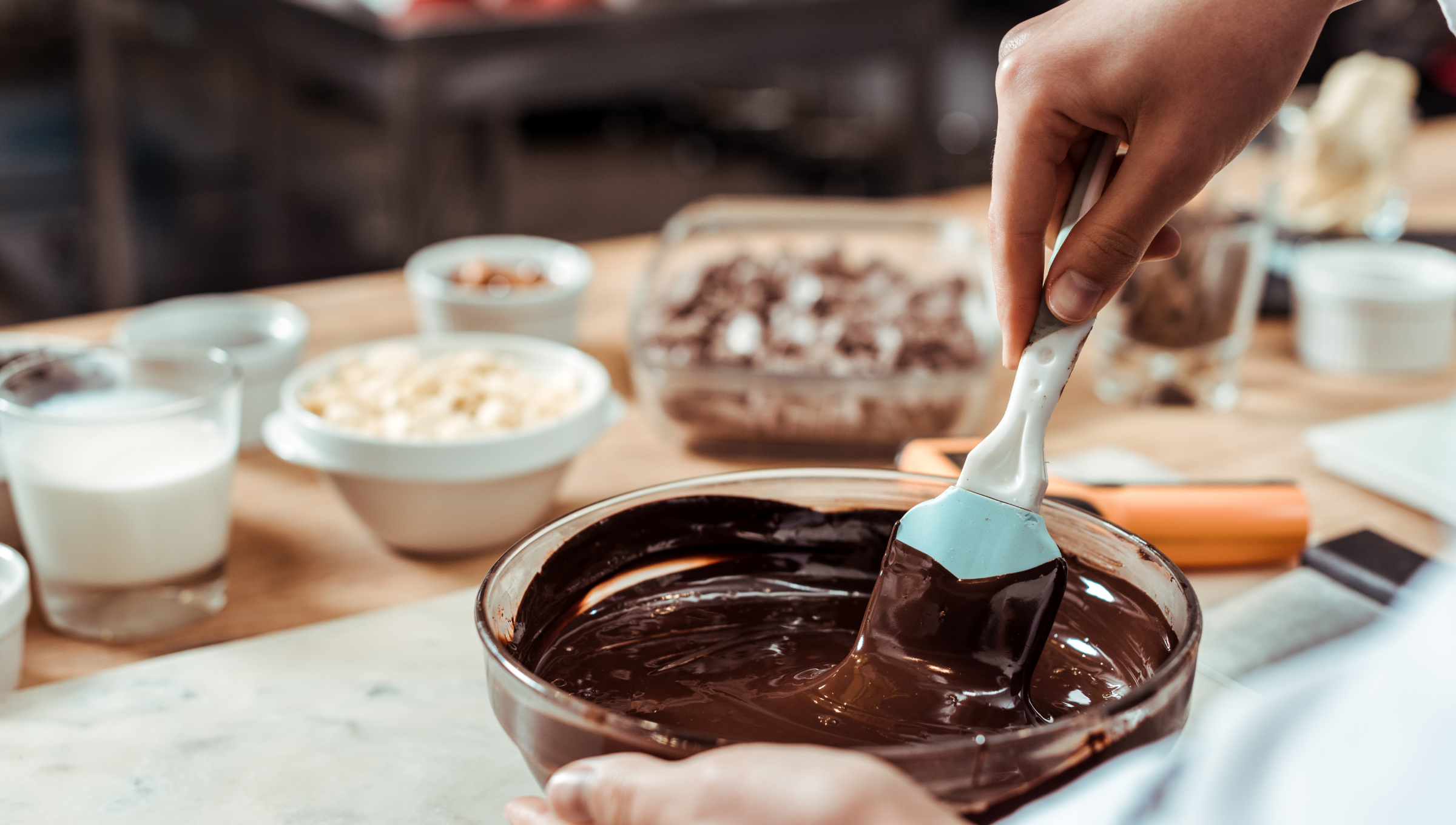 Eine Person rührt mit einem Backspatel in einer Glasschüssel mit geschmolzener Schokolade.