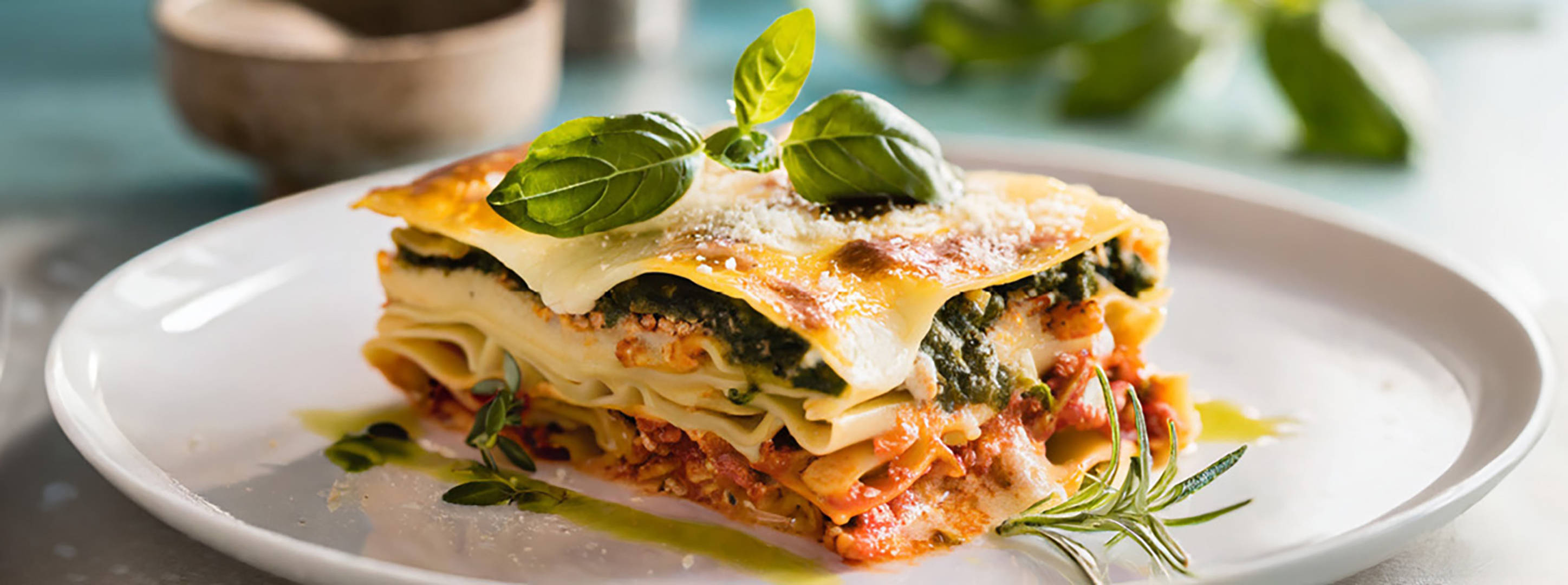 Portion Lasagne mit Käse und Basilikum auf weißem Teller.
