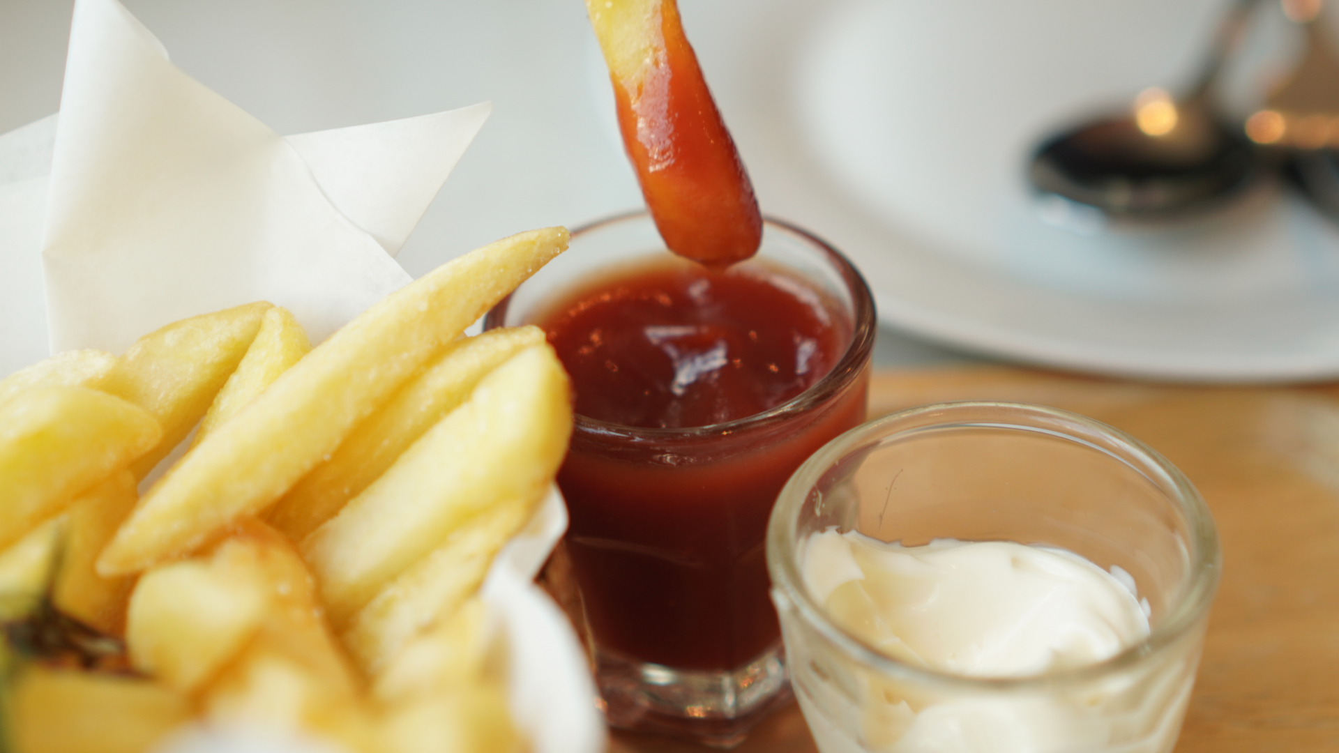 Pommes frites in Ketchup getaucht, daneben Mayonnaise.