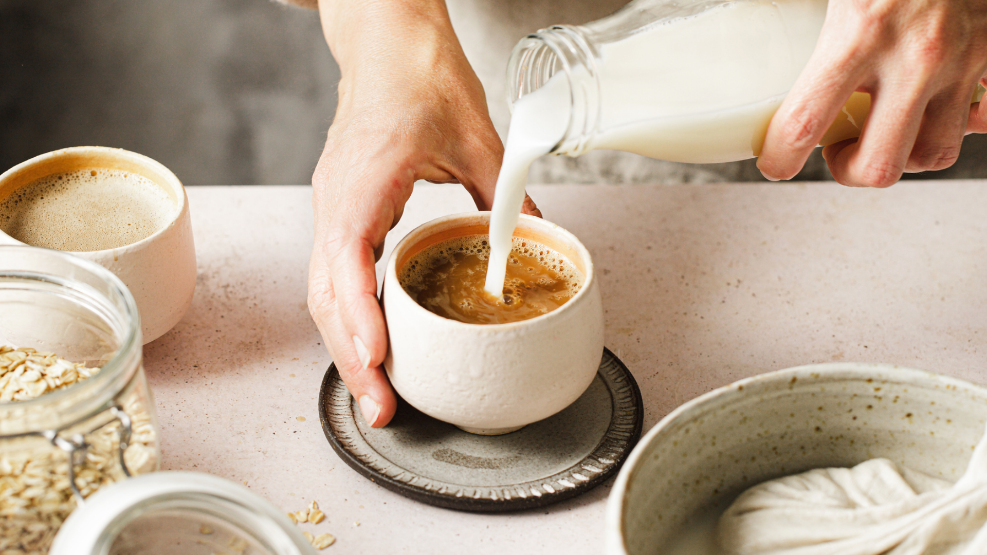 Hände gießen Milchalternative in Kaffee, Haferflocken.