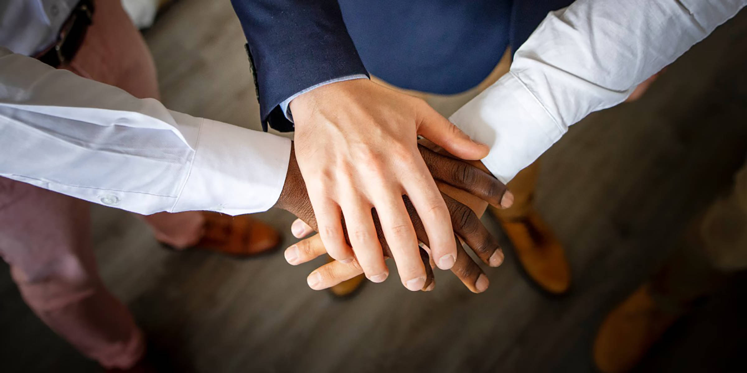 Drei Hände unterschiedlicher Personen übereinandergelegt.