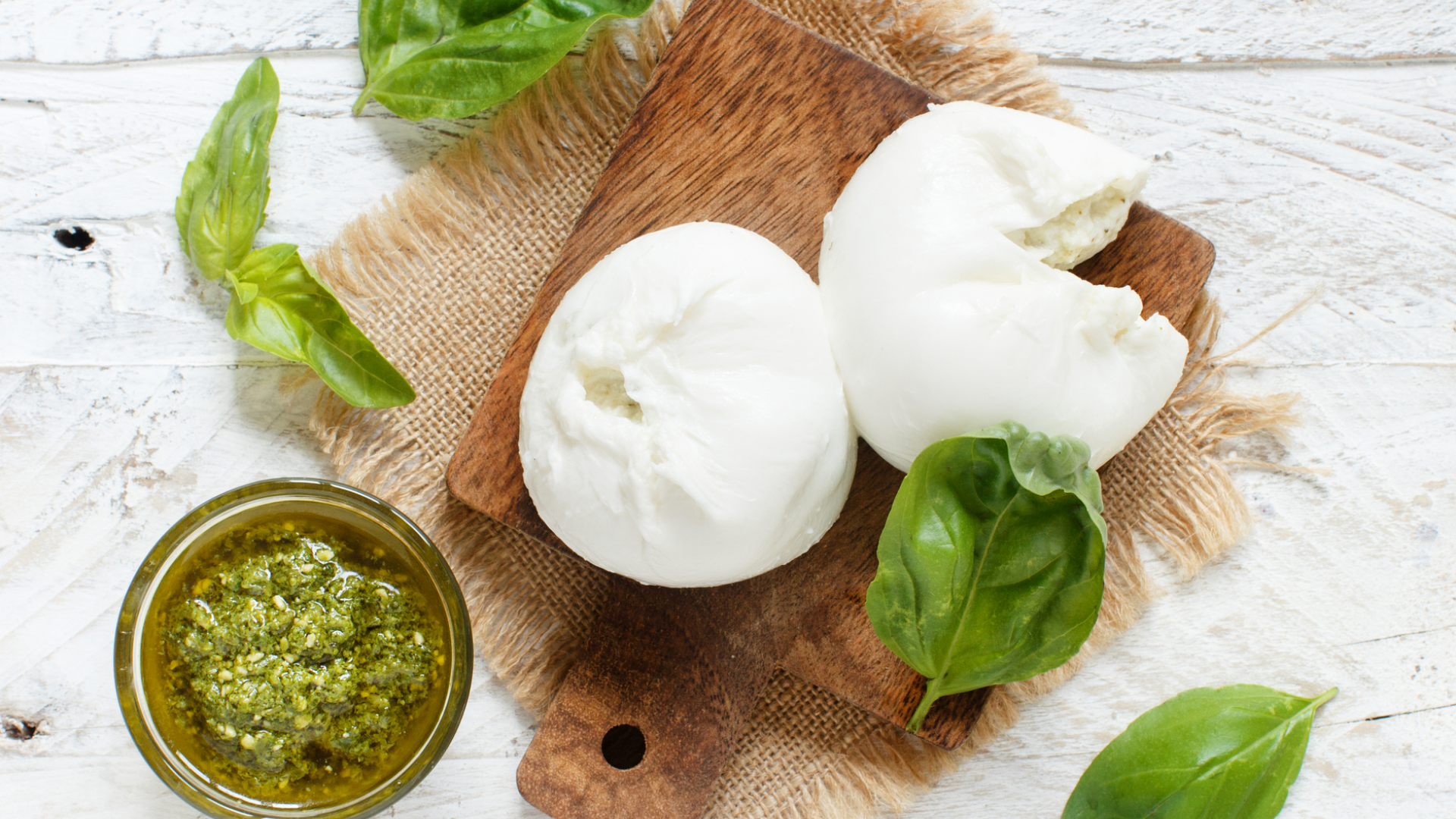 Mozzarella, Pesto, Basilikumblätter auf Holzbrett und rustikalem Hintergrund.