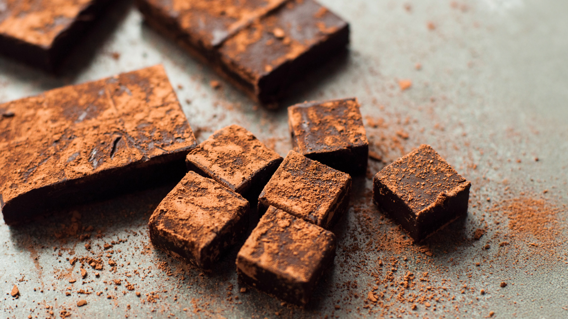 Schokoladenwürfel mit Kakaopulver auf grauem Hintergrund.